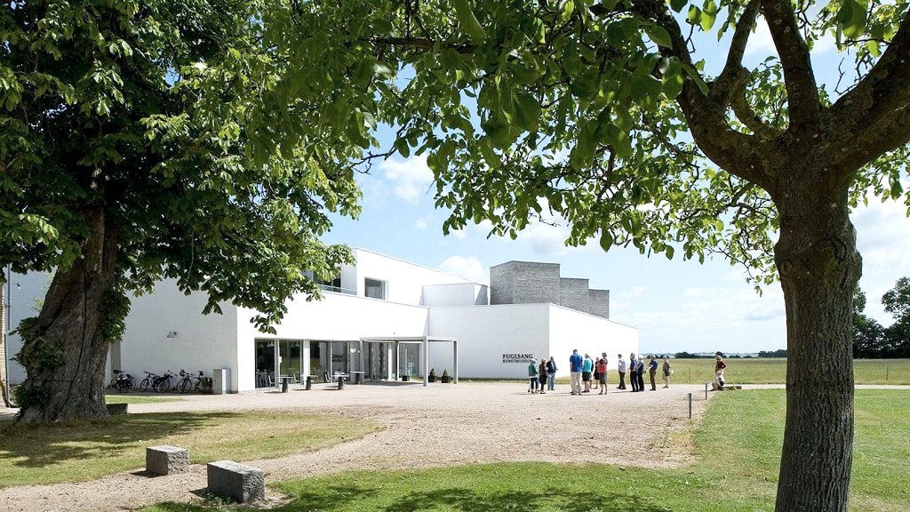 Weiße, moderne Architektur eines Museums mit Bäumen im Vordergrund und Menschen, die das Gebäude betreten.