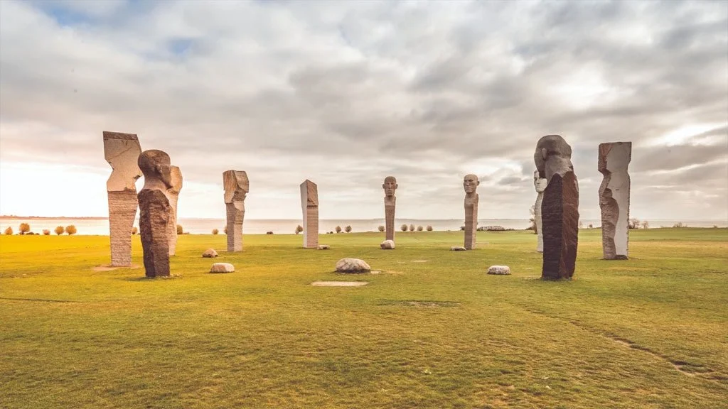 Steinskulpturen in einem Kreis auf einem grünen Feld unter bewölktem Himmel.
