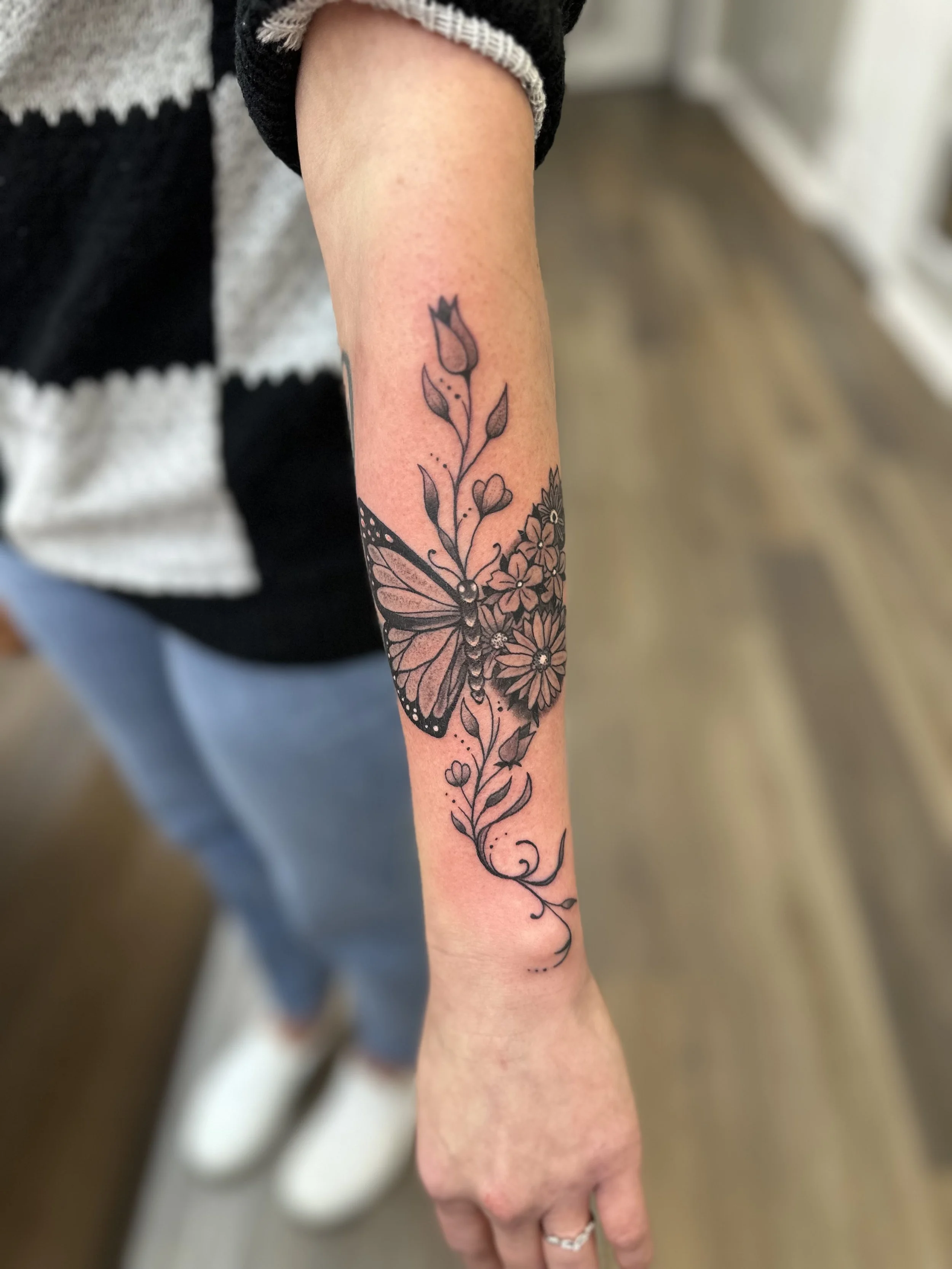 Tattoo of a butterfly surrounded by flowers on a person's forearm.