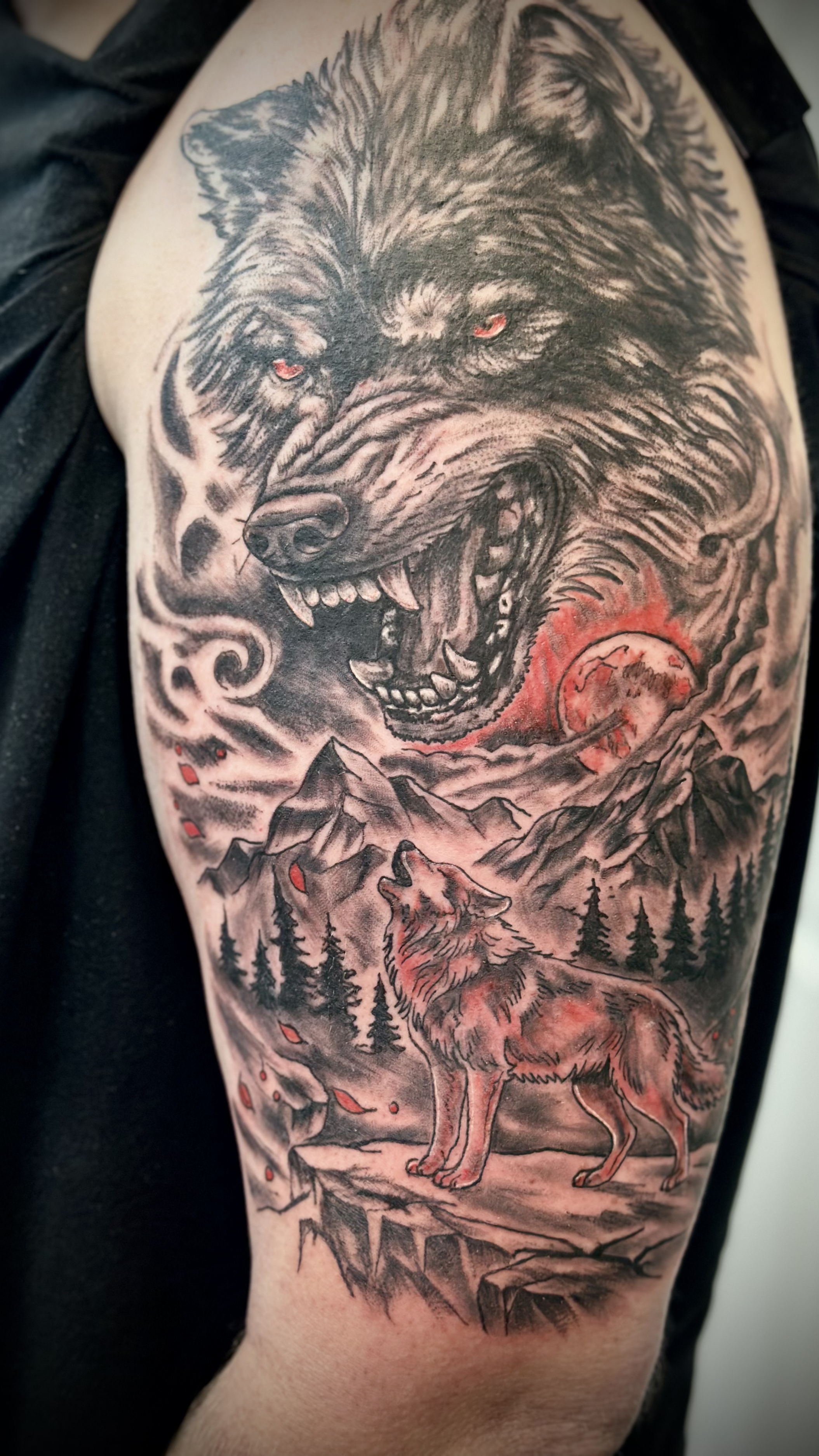 Tattoo of a fierce black wolf with red eyes, howling or snarling, set in a mountainous forest landscape with a full moon in the background and a smaller wolf at the bottom.