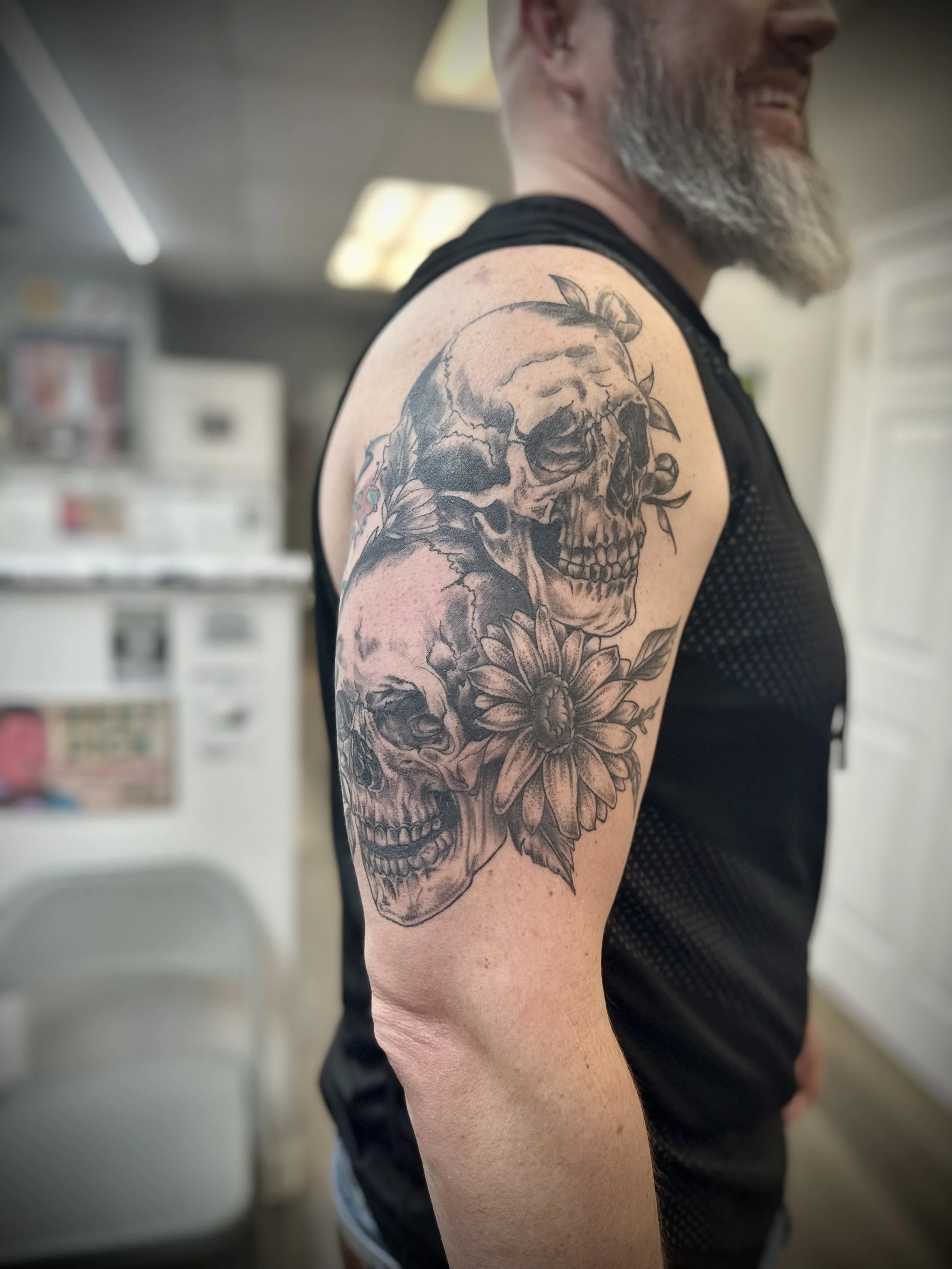 Tattoo of two skulls and a flower on a man's upper arm.