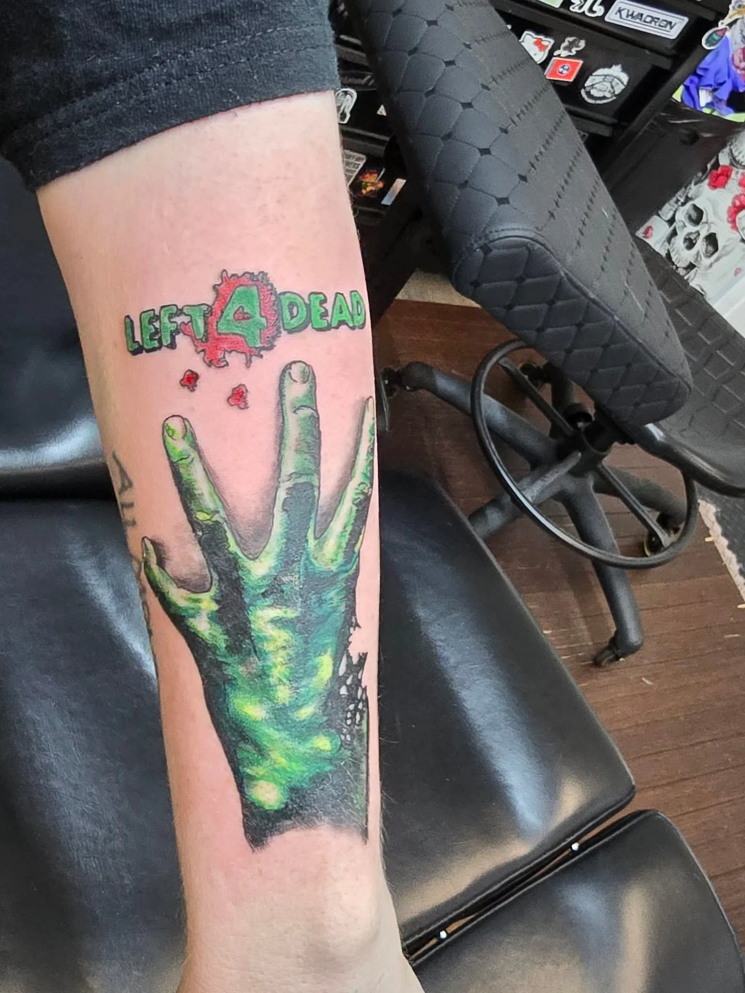 Tattoo of a zombie green hand making a peace sign, with text above reading 'Left 4 Dead' in red and green letters.