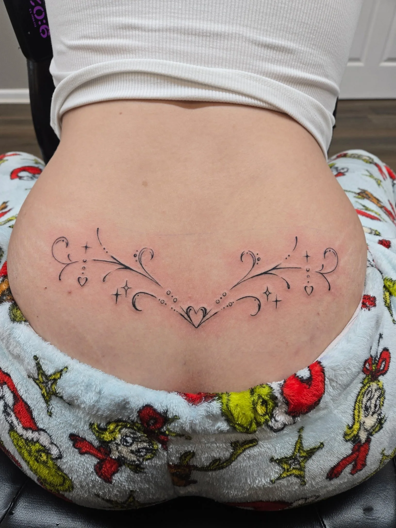 A tattoo of a decorative symmetrical heart with flourishes, stars, dots, and small hearts on the lower back.