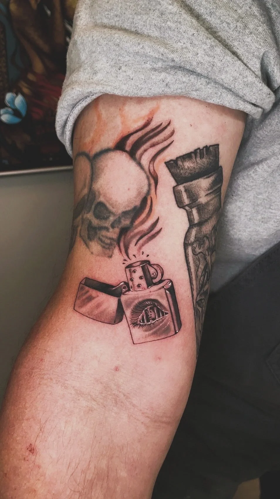 Tattoo of a skull, a lighter with an eye on its side, and a cigarette with smoke.