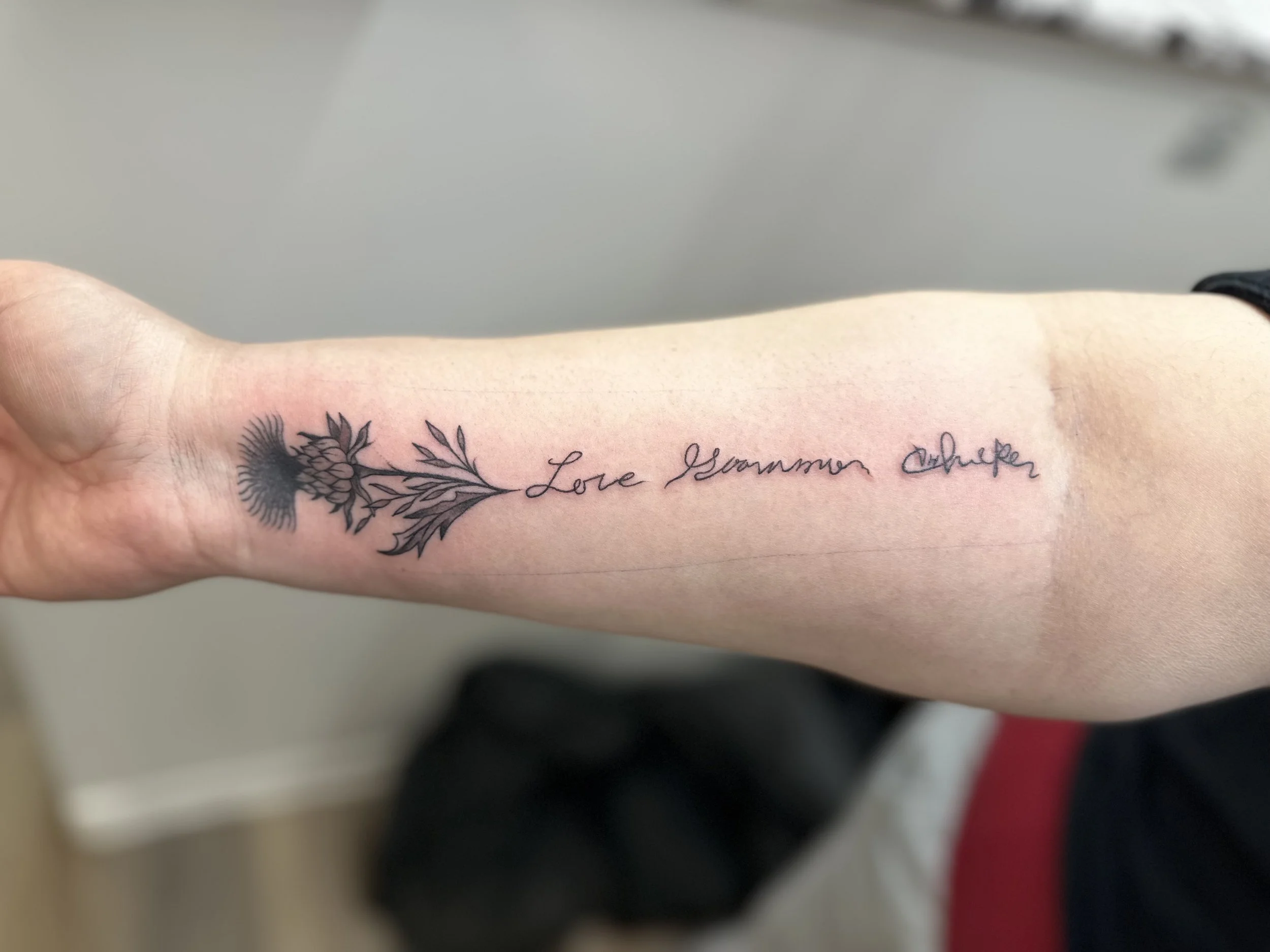 Tattoo on forearm with a flower and leaves design, and the words 'Love Grows More' written in cursive.