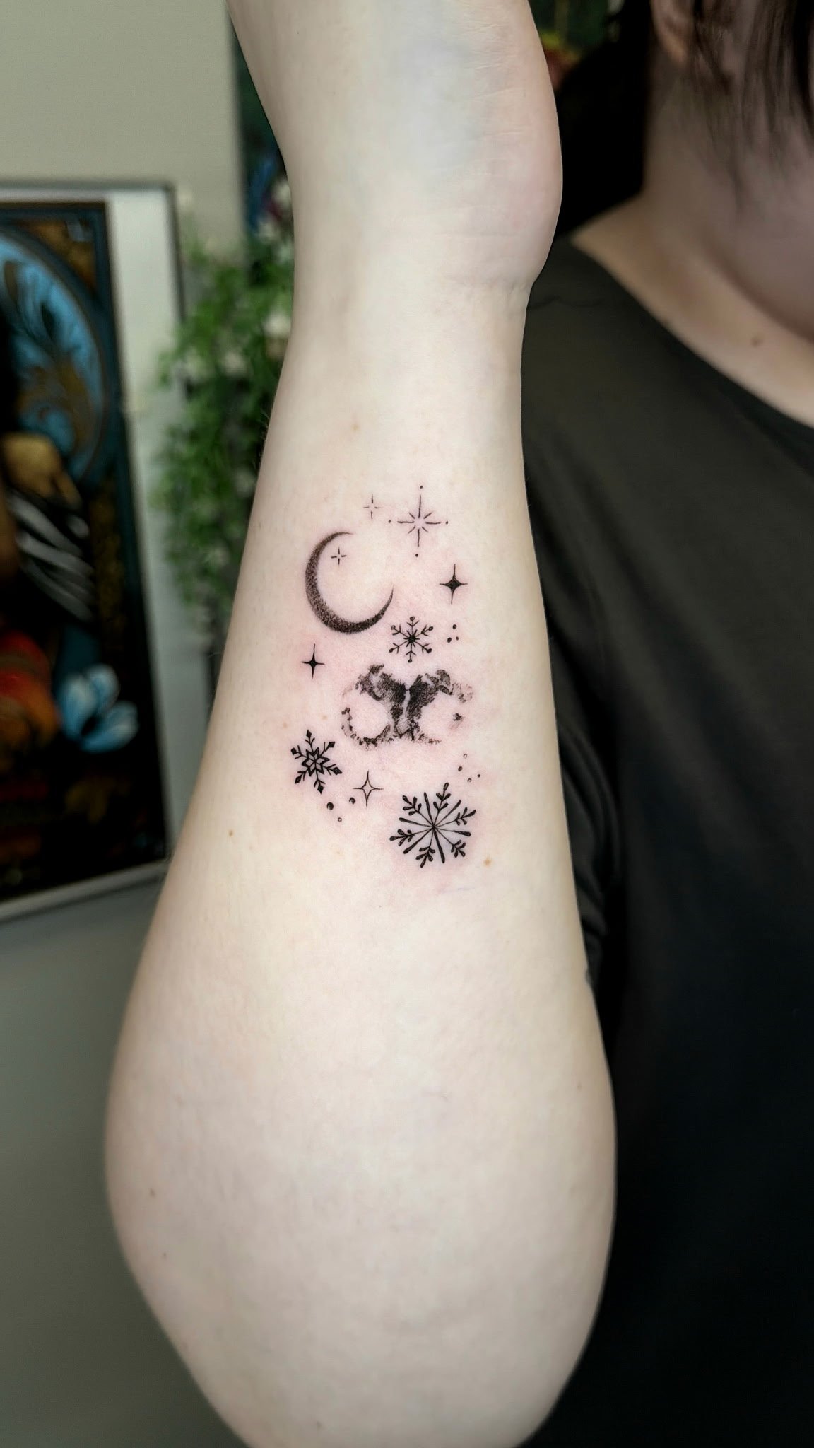 Tattoo of a moon, stars, snowflakes, and abstract designs on a person's inner forearm.