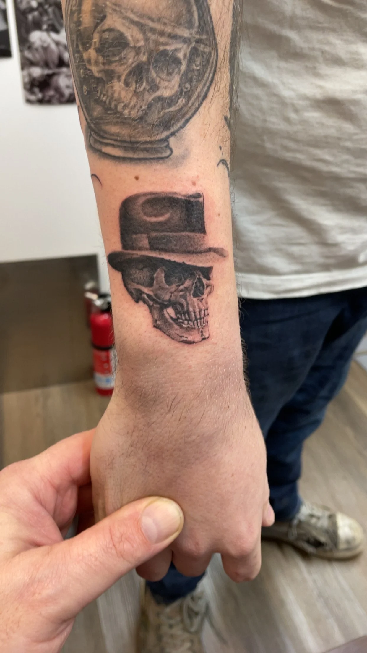 Tattoo of a skull wearing a fedora hat on a person's forearm.