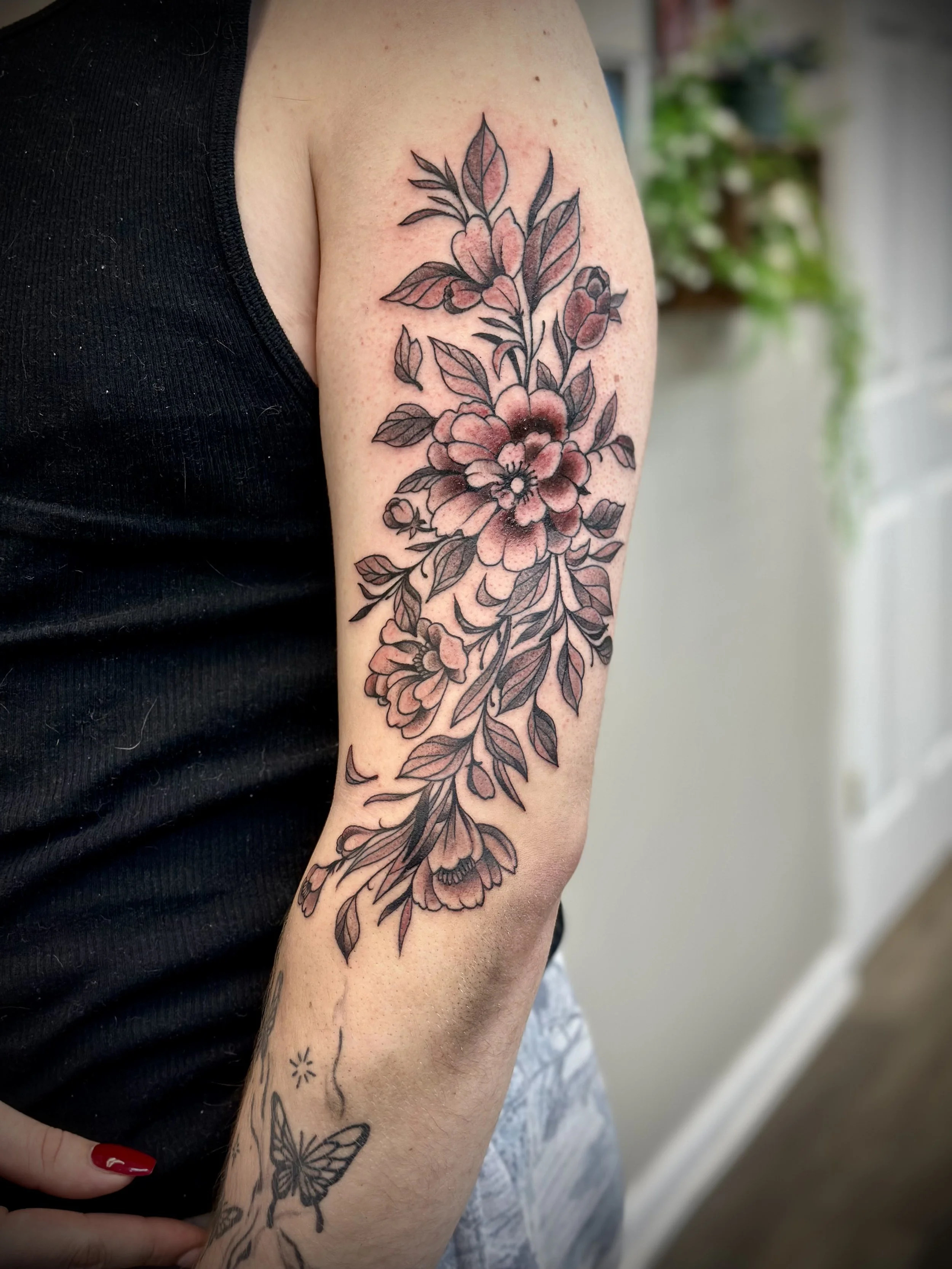 Tattoo of pink and black flowers and leaves on person's upper arm.
