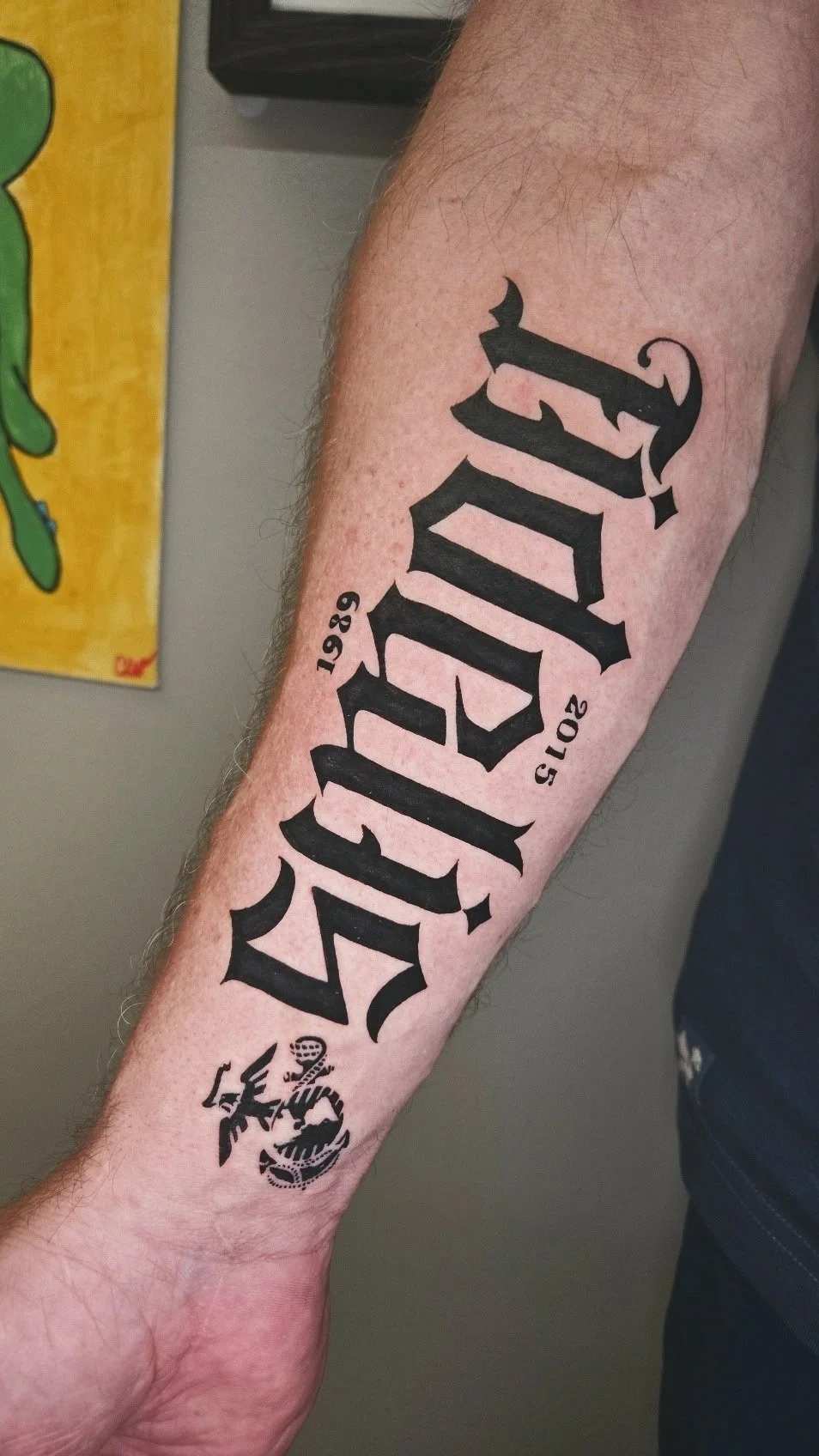 Tattoo on forearm with the word 'PRIDE' in prominent black gothic font, along with the years '2019' and '2015', and a small black emblem resembling a snake and skull.
