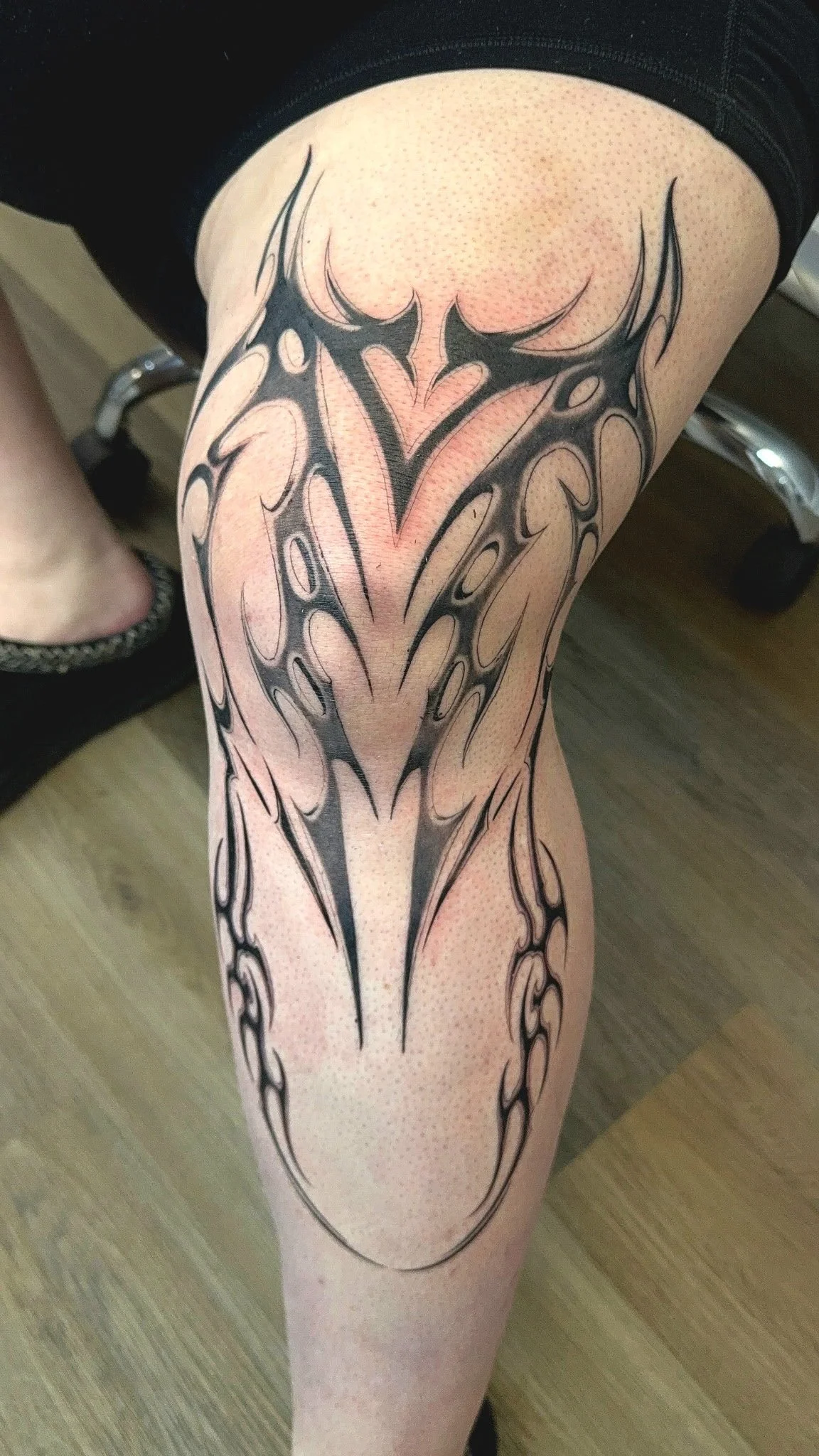 A person's leg with a large black tribal-style tattoo extending from the thigh to below the knee.