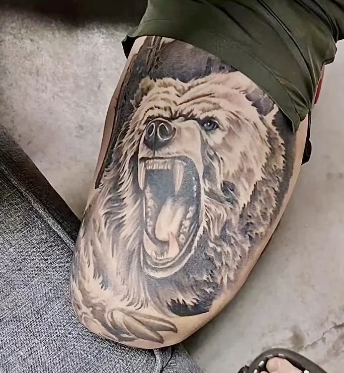 Tattoo of a snarling bear on a person's thigh