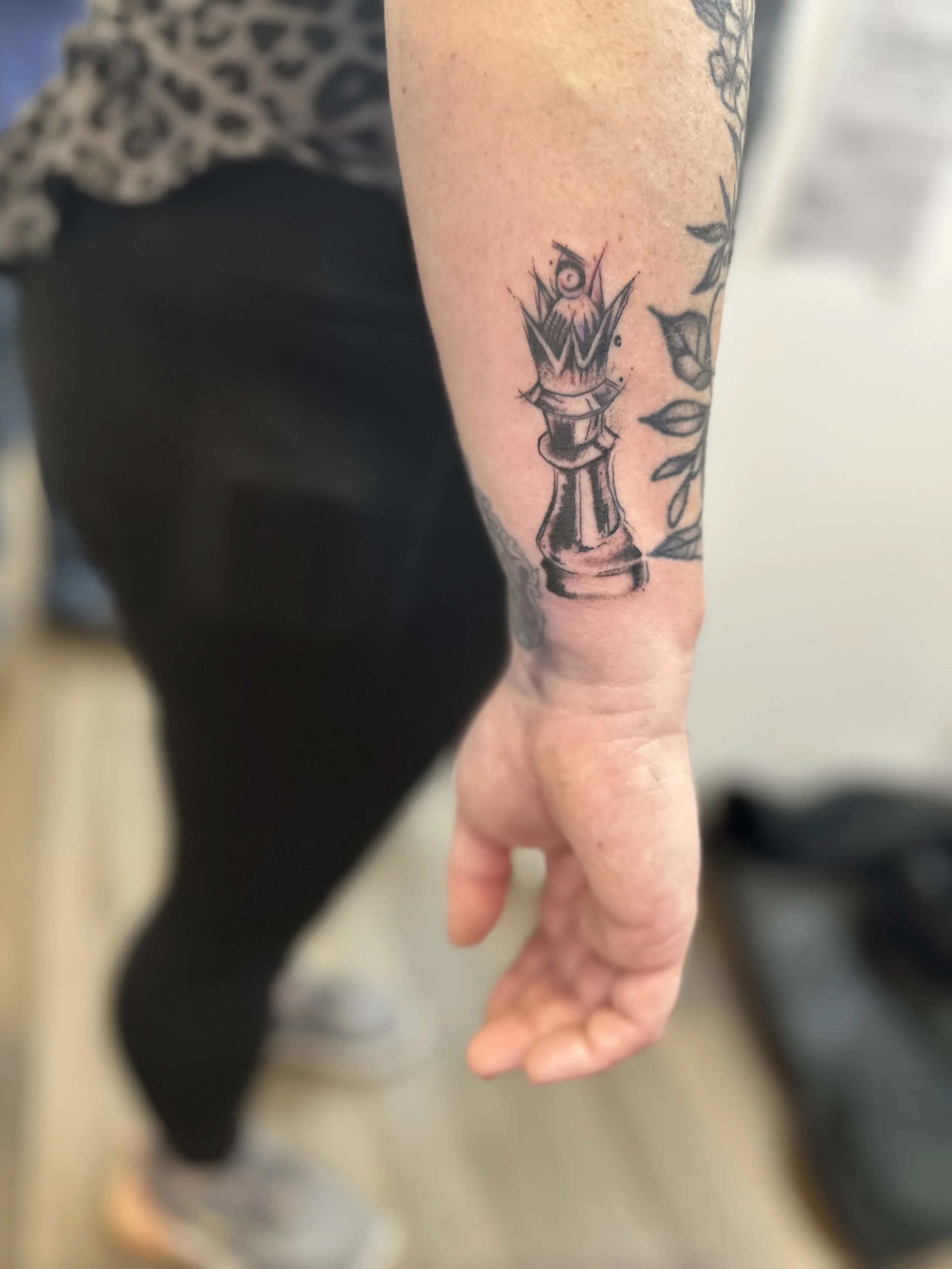 Tattoo of a chess rook with flames and a crown on the person's forearm.
