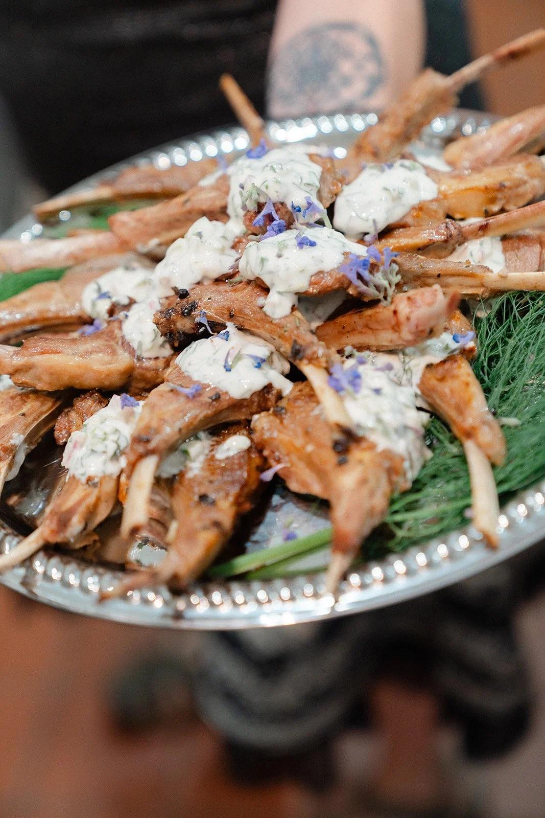 Plate of grilled lamb chops topped with a creamy herb sauce and edible flowers, garnished with green herbs.