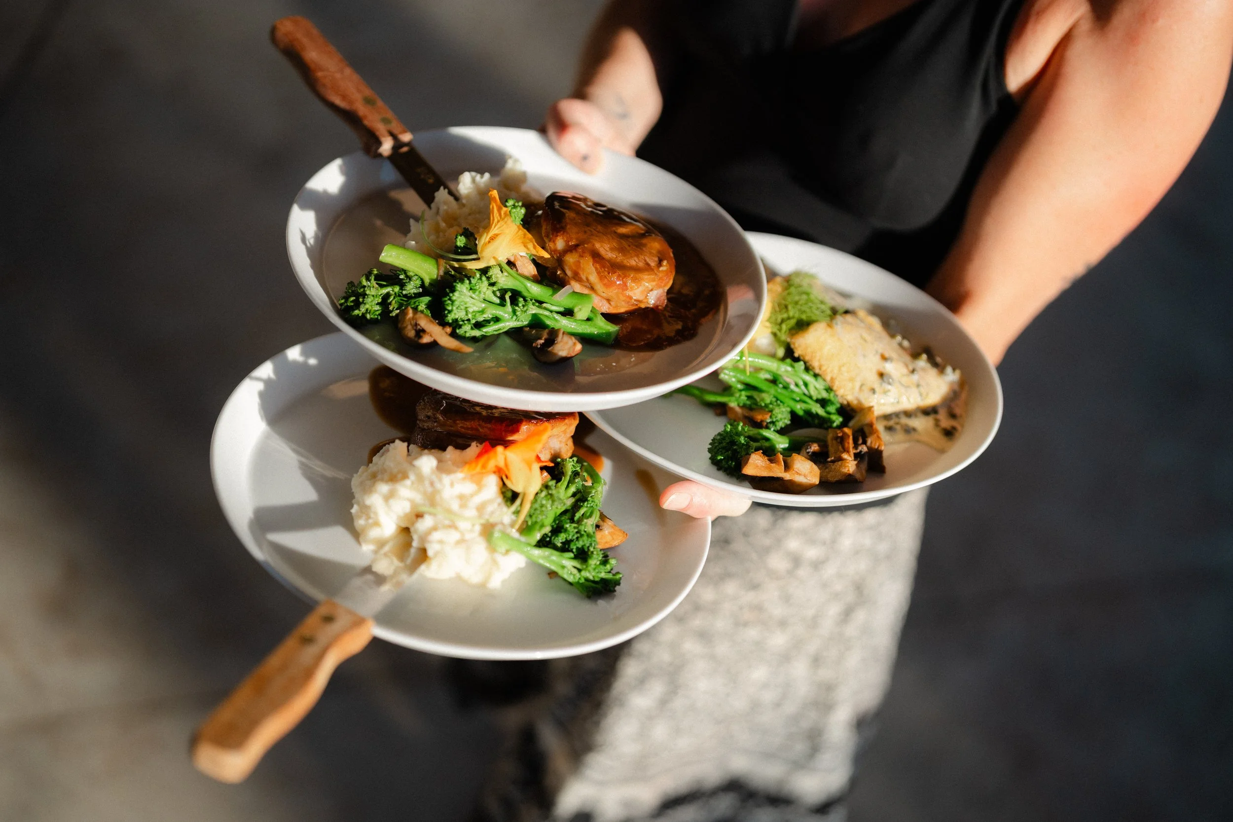 Person serving plates of assorted food including vegetables, mashed potatoes, and a piece of meat with sauce.