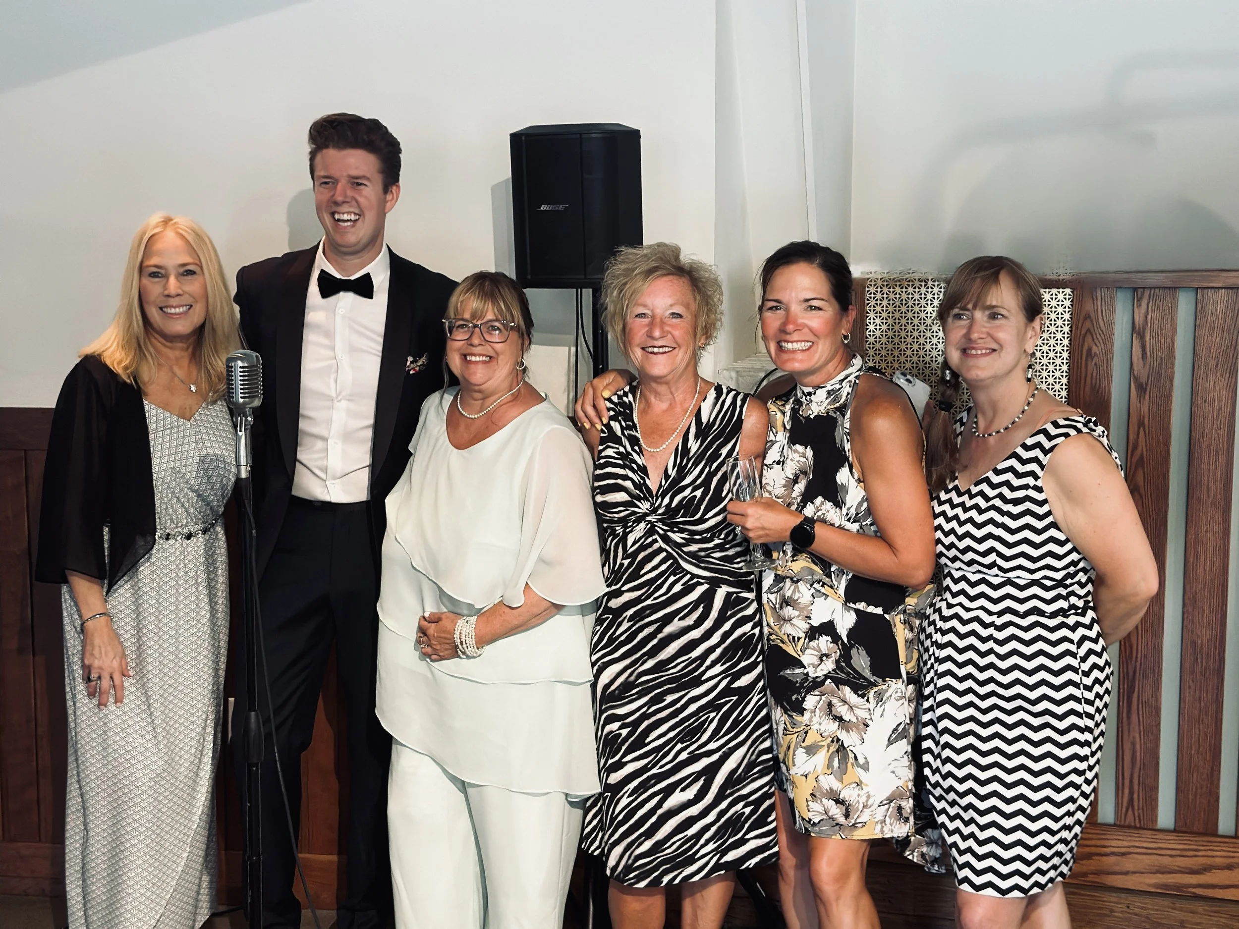 Group of six people at a celebration, dressed in formal attire, standing together and smiling in front of a wall at the Starling in Milwaukee, Wisconsin