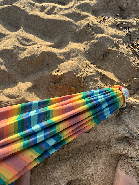 Colorful striped beach umbrella lying on sandy beach.