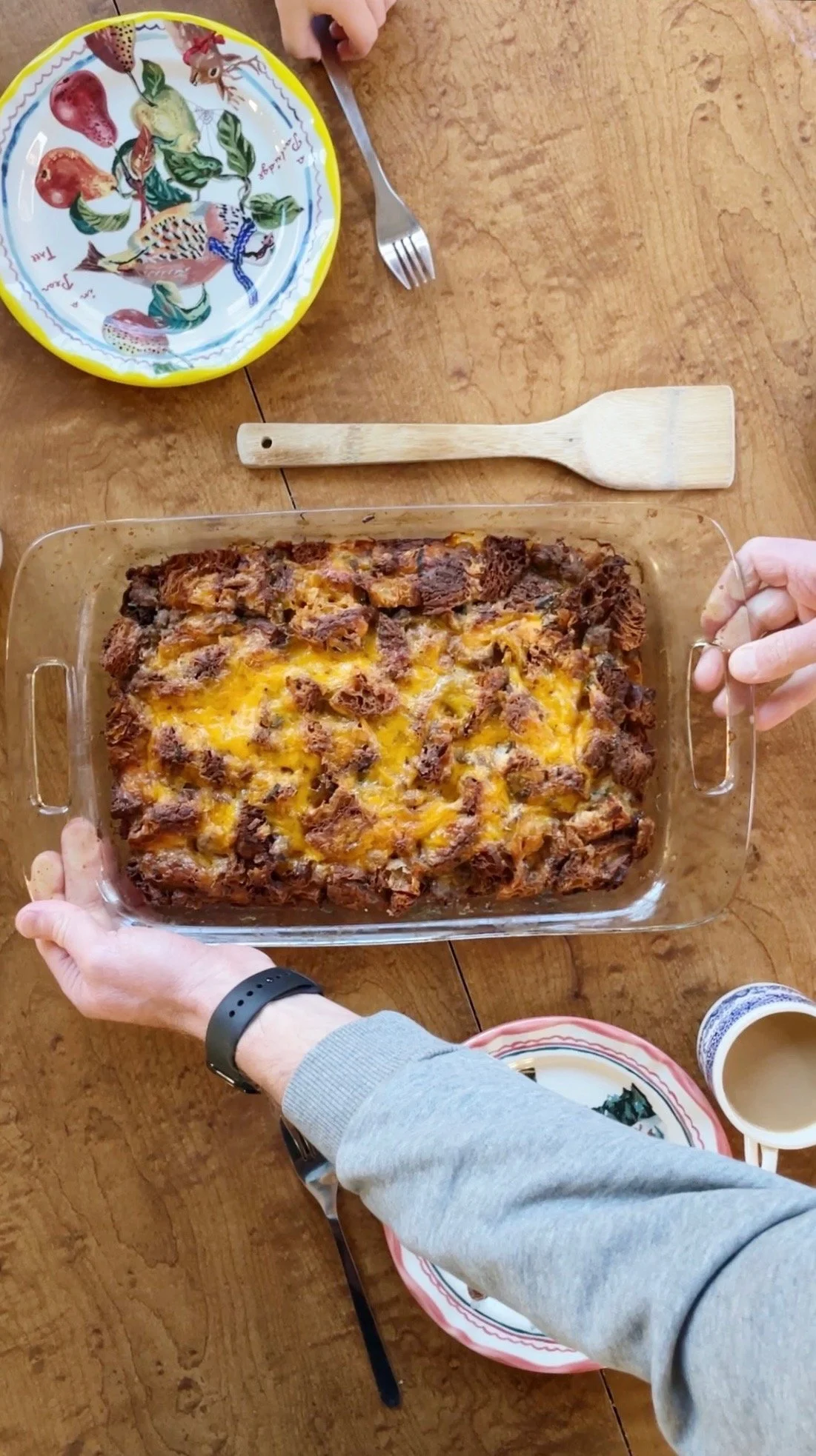 Person holding a glass casserole dish filled with baked beef and cheese casserole on a wooden table.