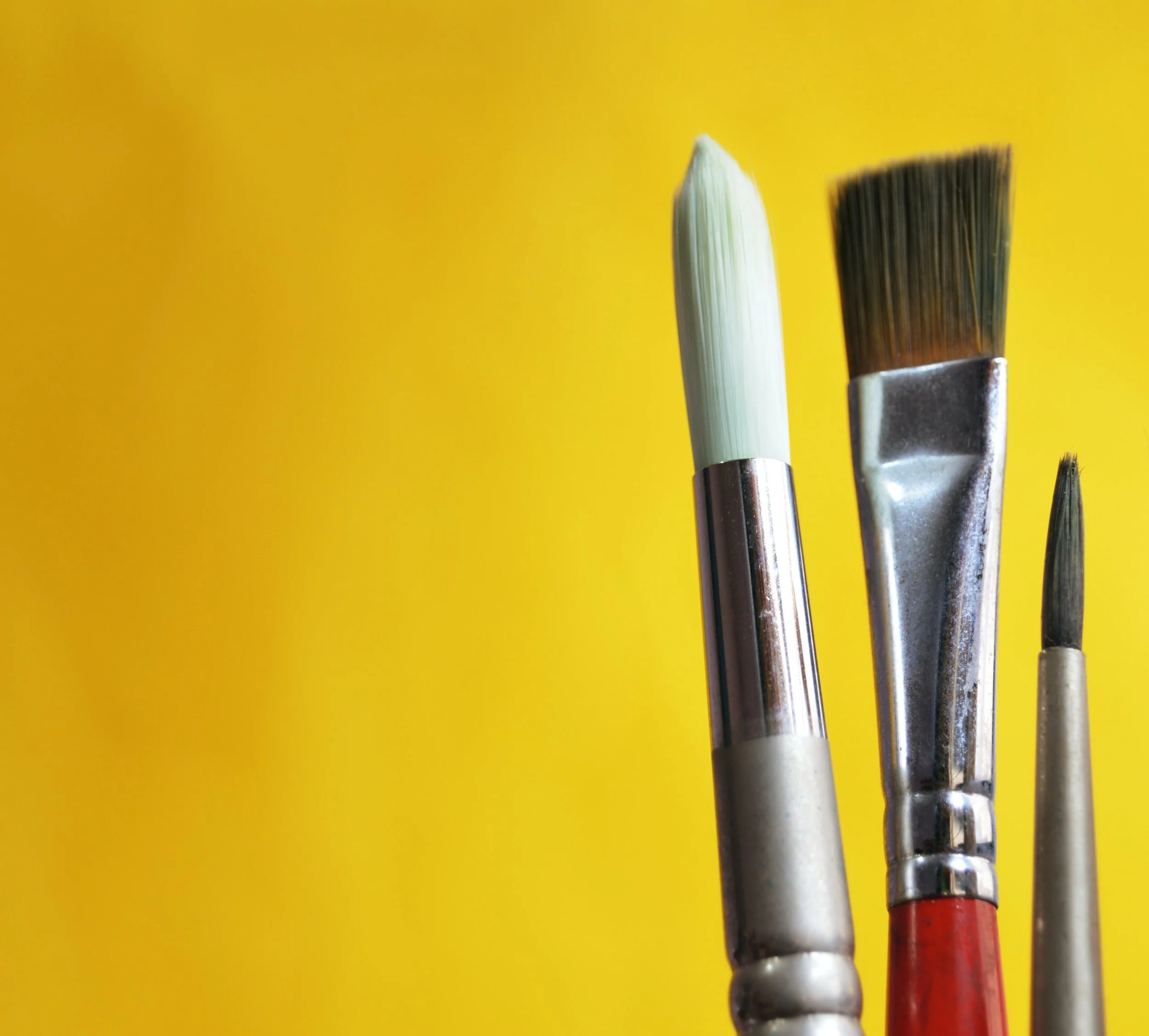 Close-up of paintbrushes with colorful handles, set against a bright yellow background.