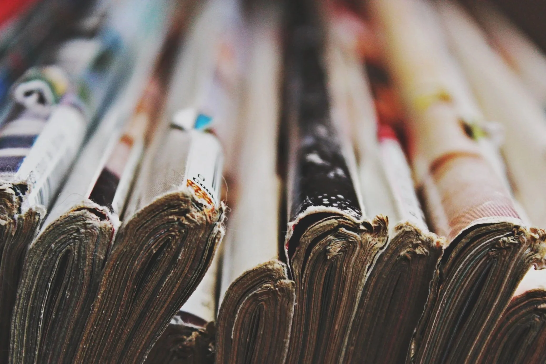 Close-up of rolled magazines or newspapers arranged in a row, with visible rough edges and colorful spines.