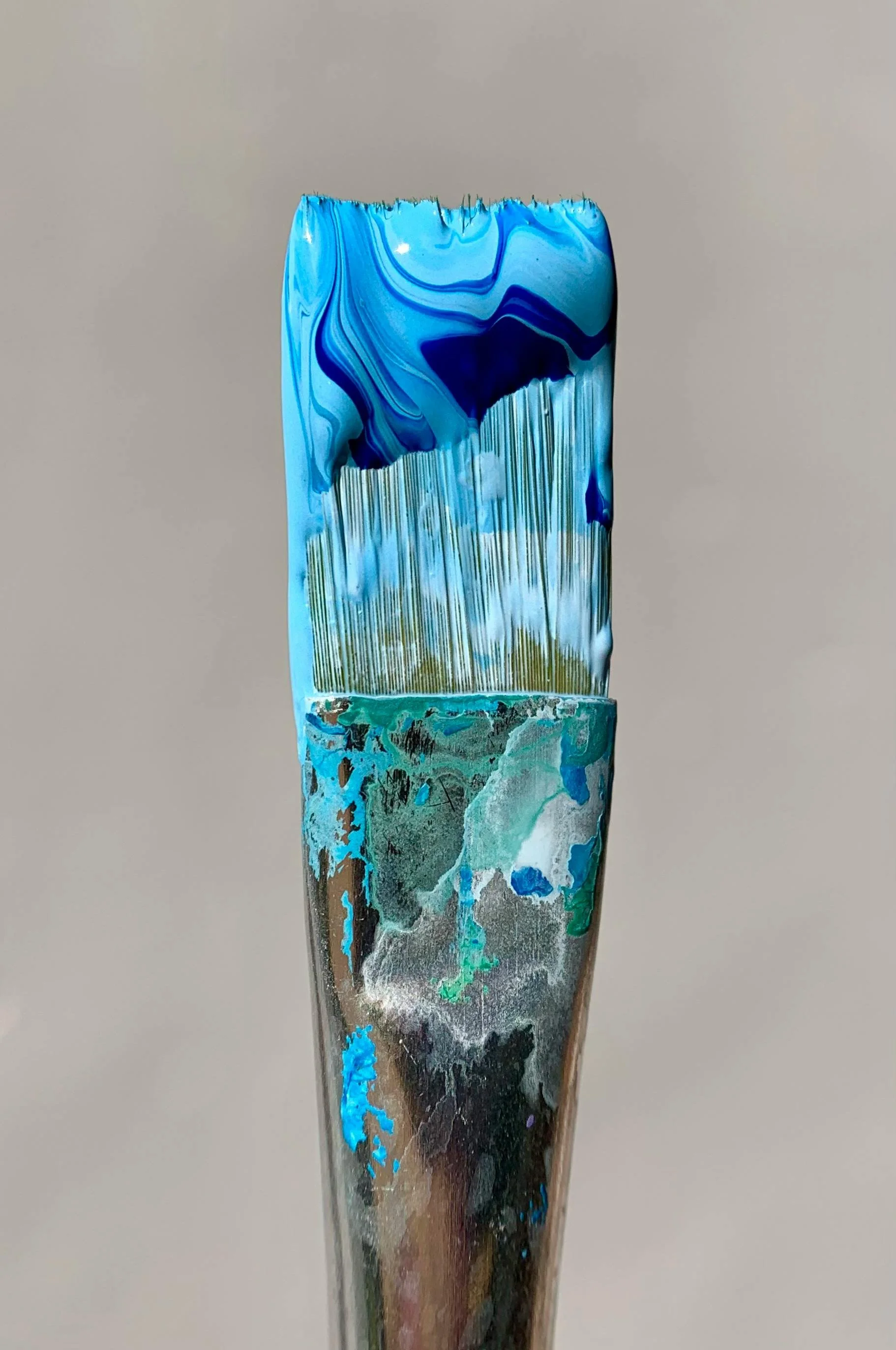 Close-up of a paintbrush with blue abstract paint on the bristles and handle.