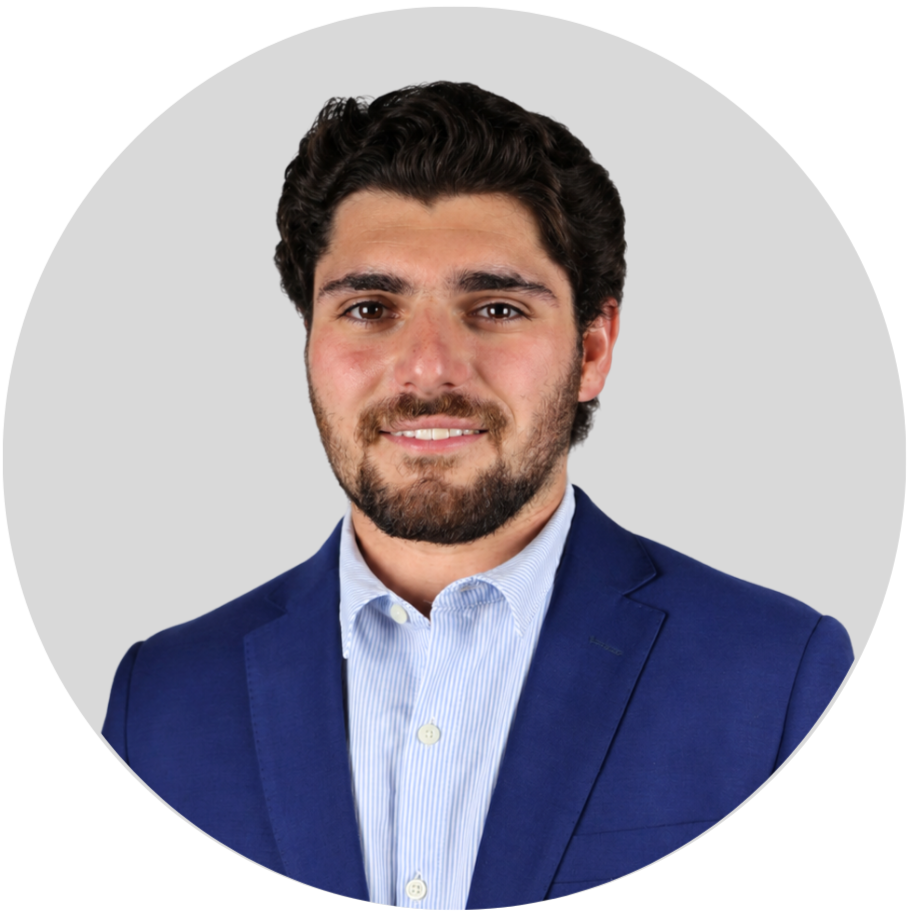 Portrait of a young man with dark hair and beard wearing a blue suit and light blue shirt, smiling at the camera.
