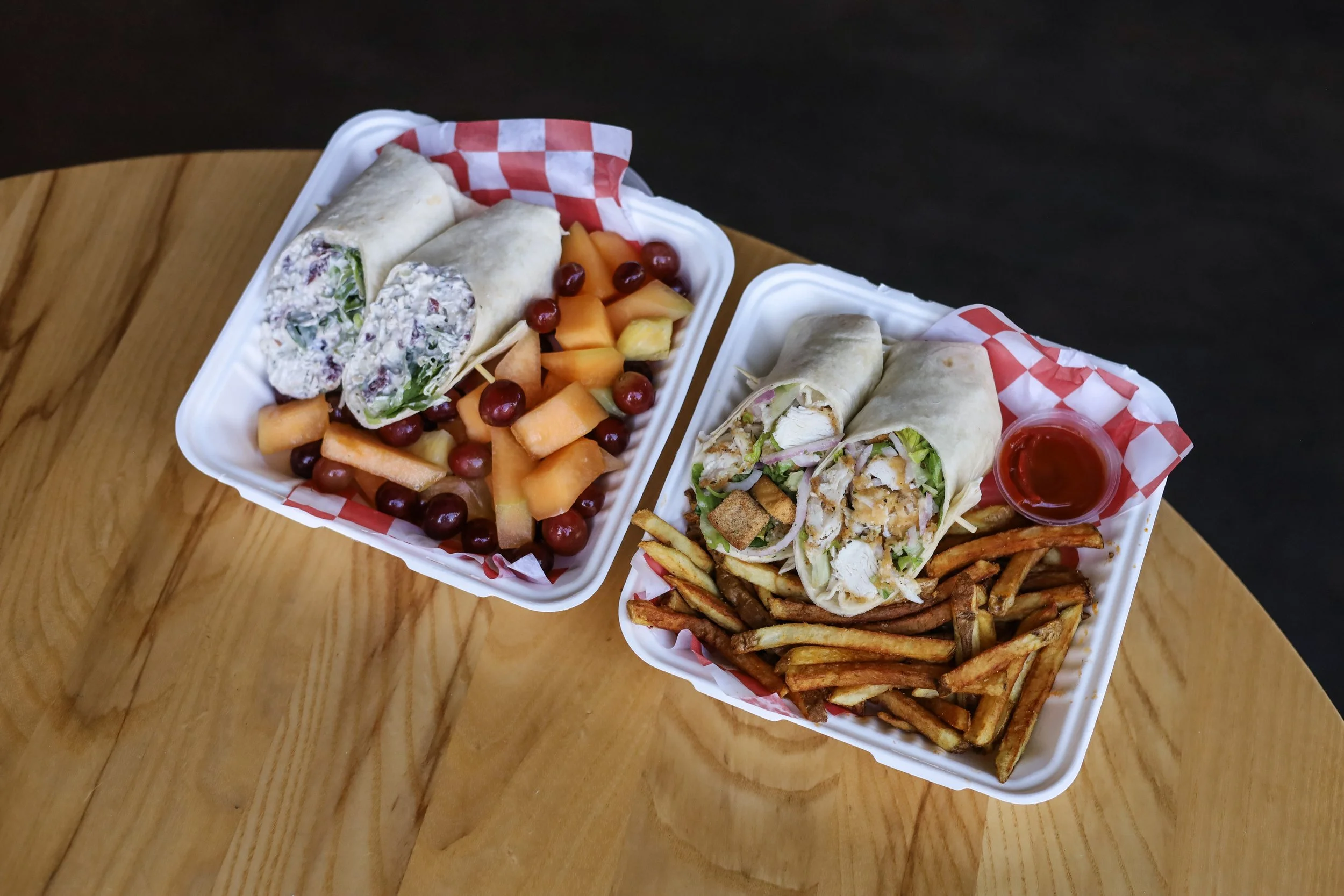 Two containers each holding a chicken wrap and a side.