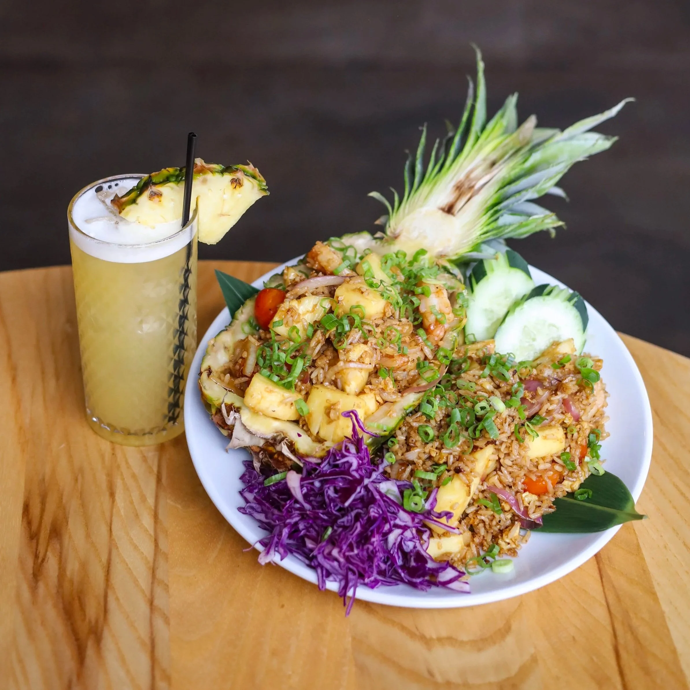Pineapple shrimp fried rice served in an empty pineapple alongside a fruity cocktail with a pineapple garnish
