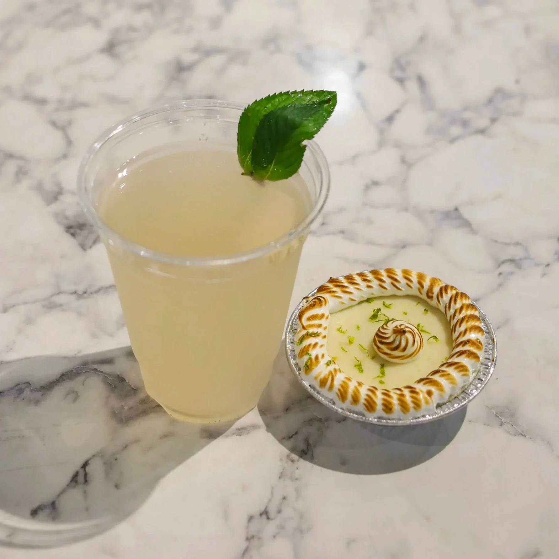 A cup of lemonade next to a mini pie on a granite counter top.
