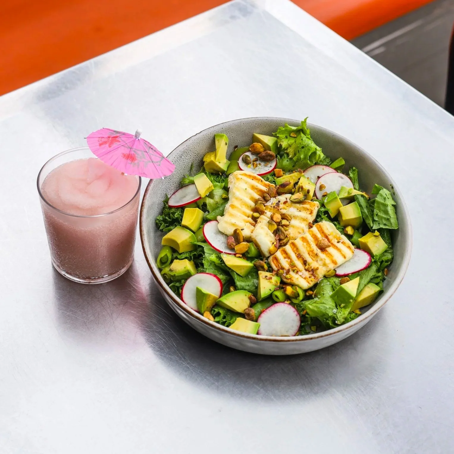 An outdoor table holding a halloumi salad and a frozen wine slushie.