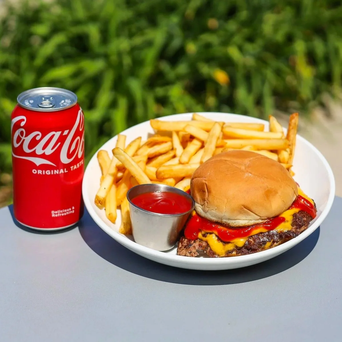 Cheeseburger with ketchup in a bun served with French fries on a white plate.