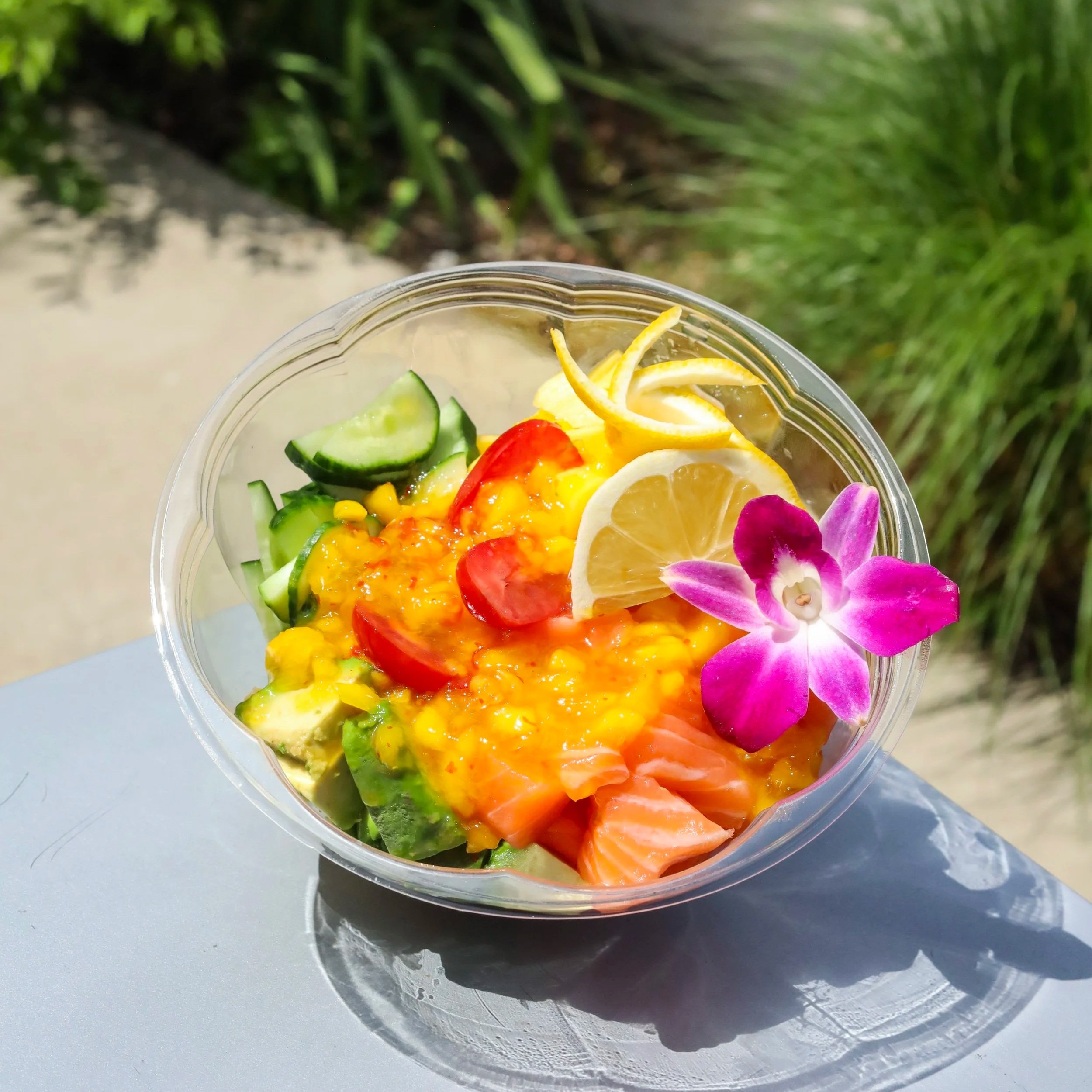 A poke bowl filled with veggies, raw salmon, mango, and colorful flowers.