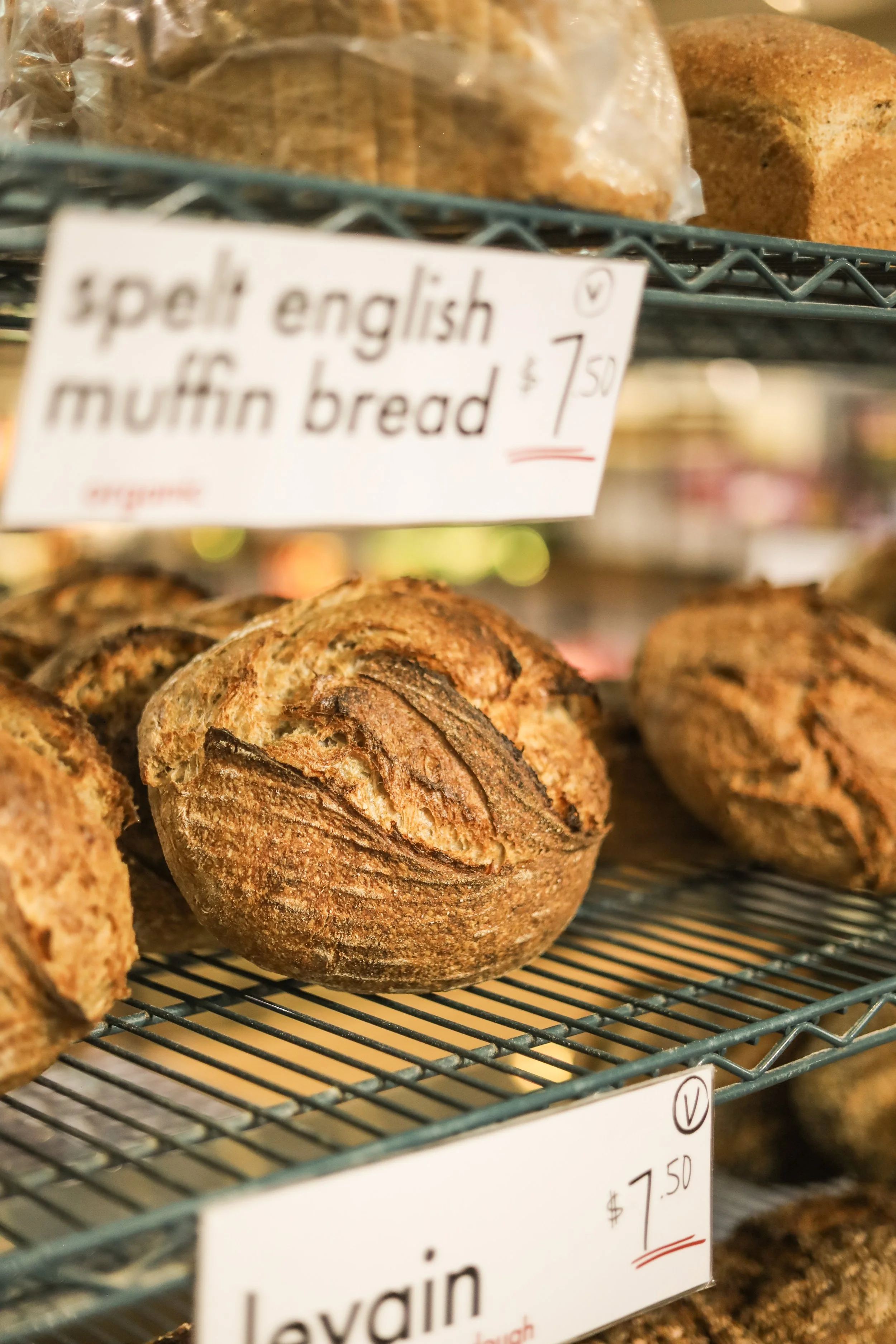Close-up of a baked English muffin bread on a wire rack in a bakery, with a hand-written price tag of $7.50 seen in the background.