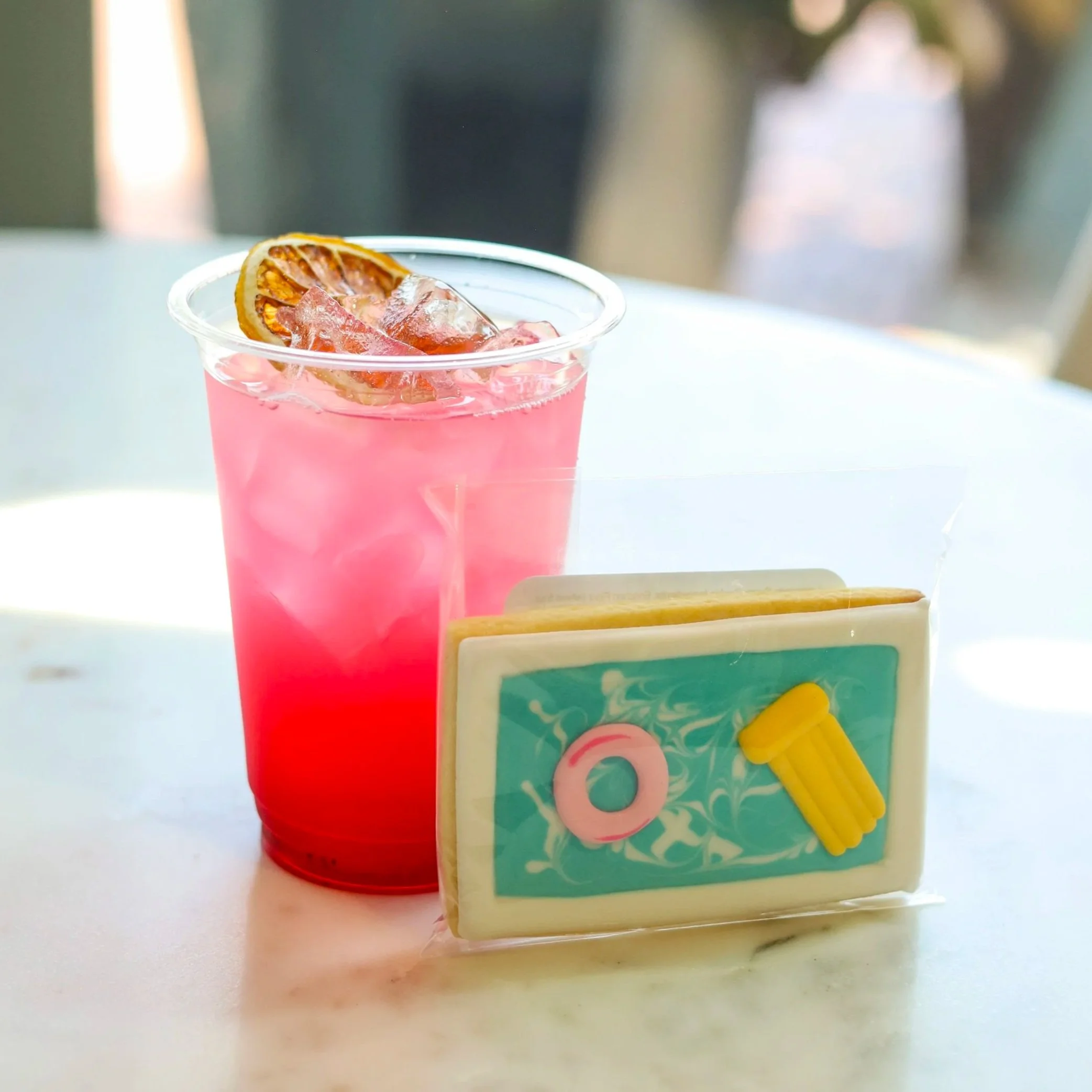 A pink lemonade next to a cookie decorated like a swimming pool.