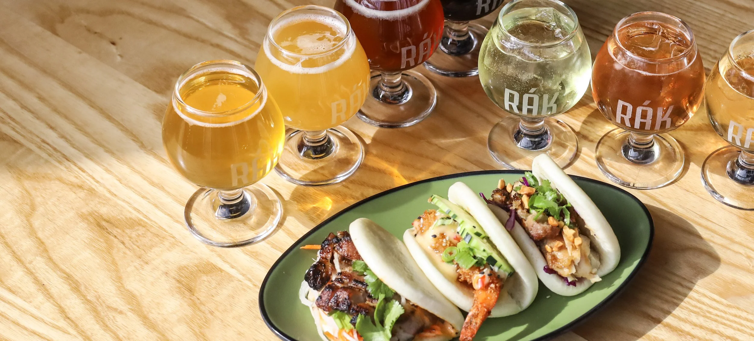A table filled with beverage flights and a bao bun trio from Rák Thai