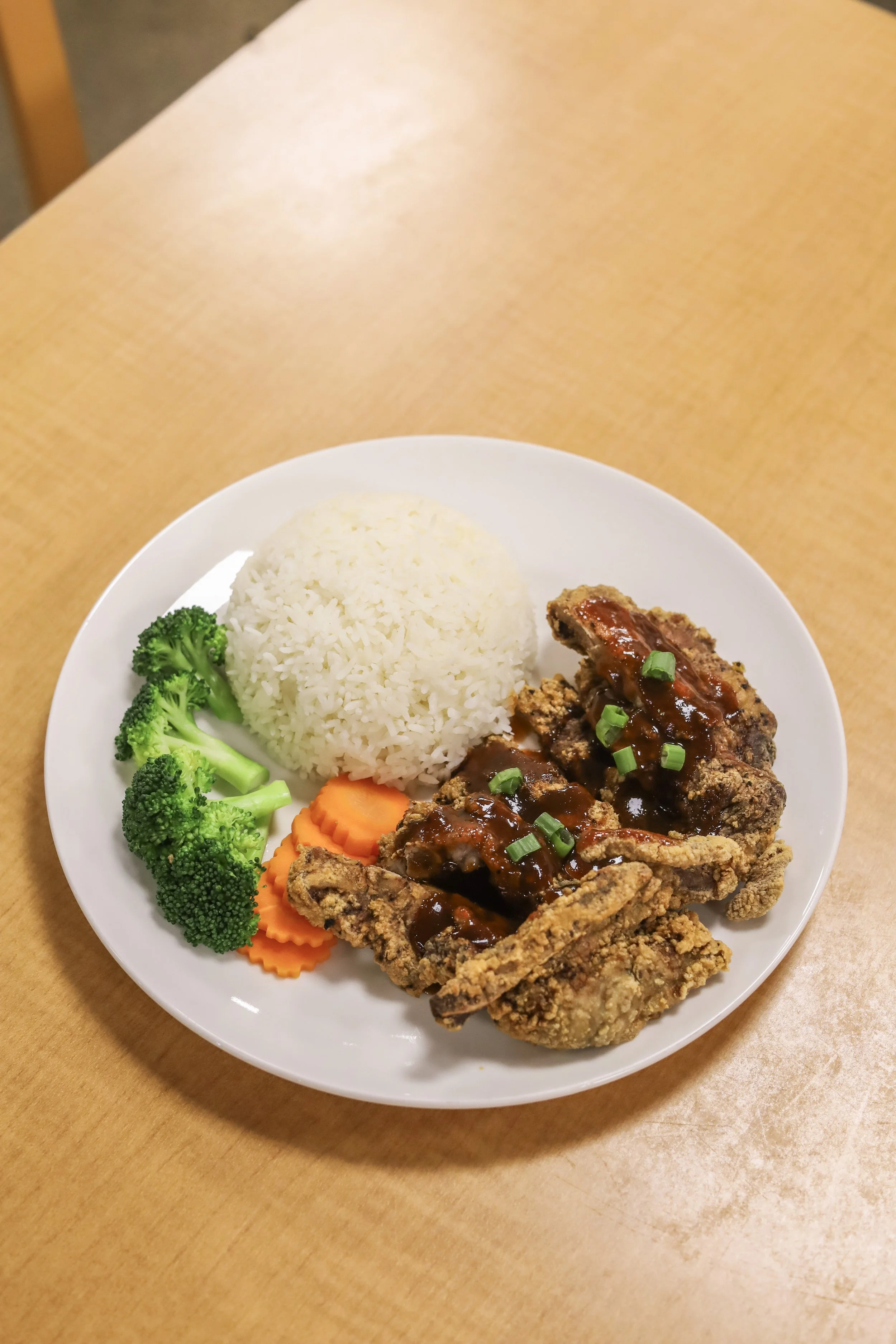 Plate of food crispy pork, white rice, broccoli, sliced carrots, and sauce with chopped green onions.
