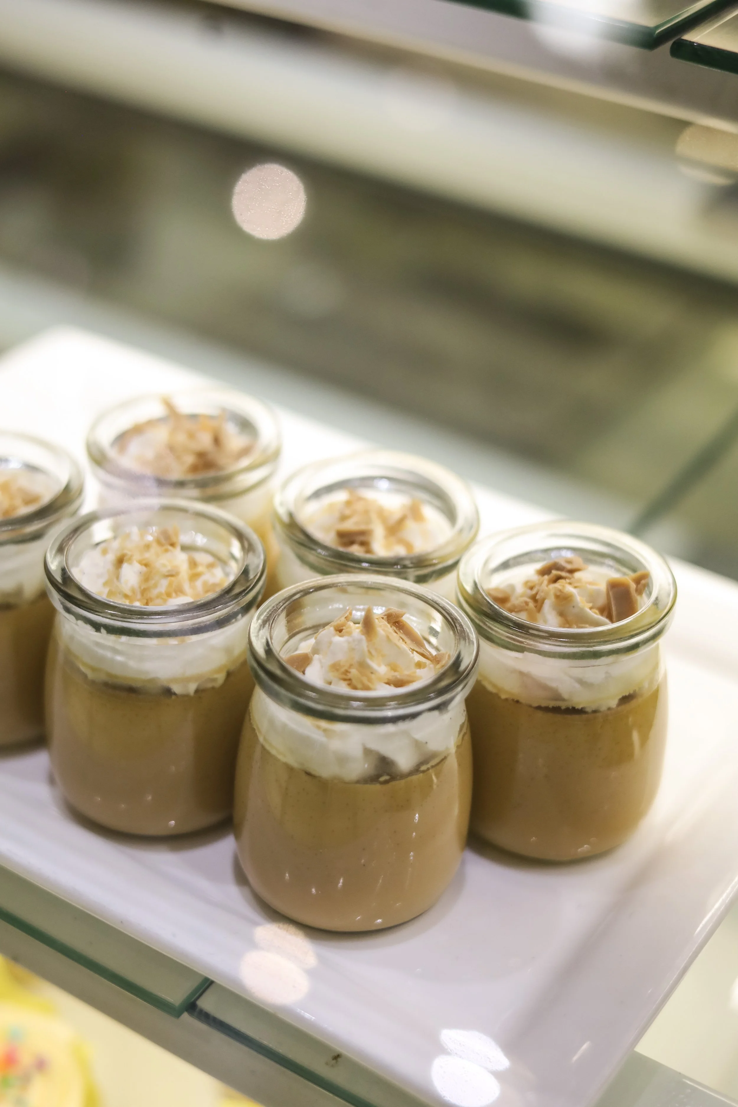 Glass jars filled with a creamy dessert topped with whipped cream and chopped nuts, displayed on a white platter.