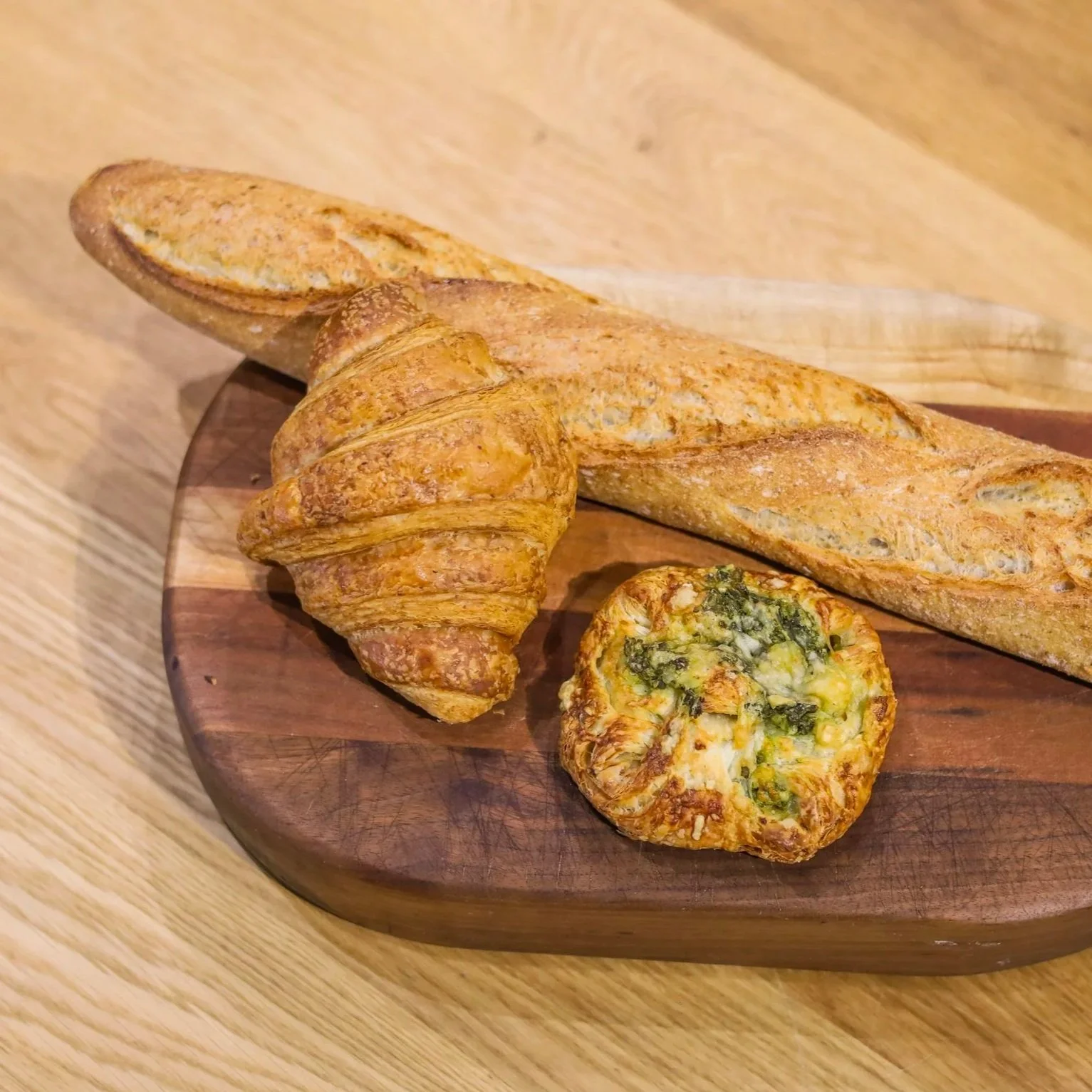 A wooden cutting board with two croissants and a fresh baguette.