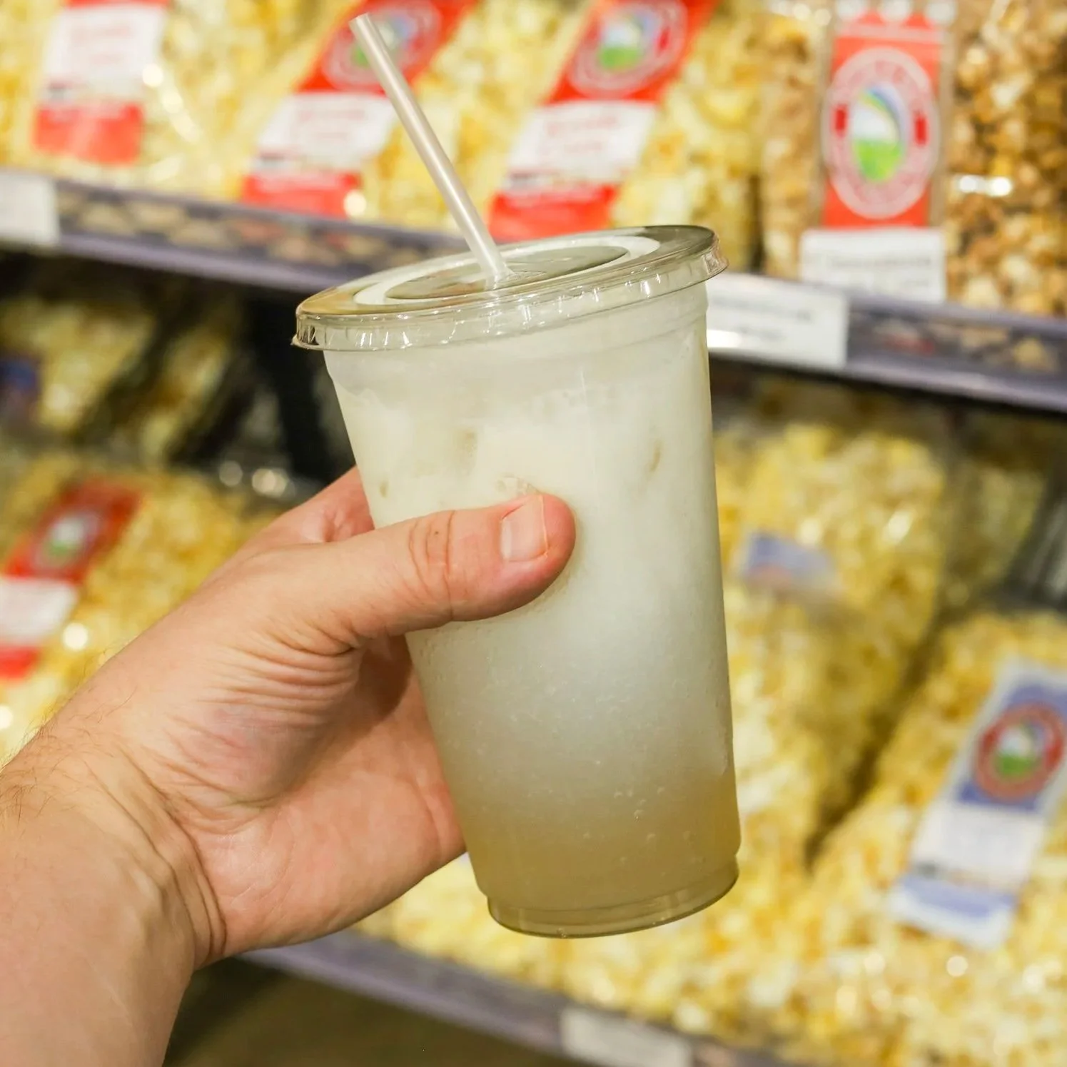 A cup of soda with added vanilla cream in front of a shelf of popcorn.
