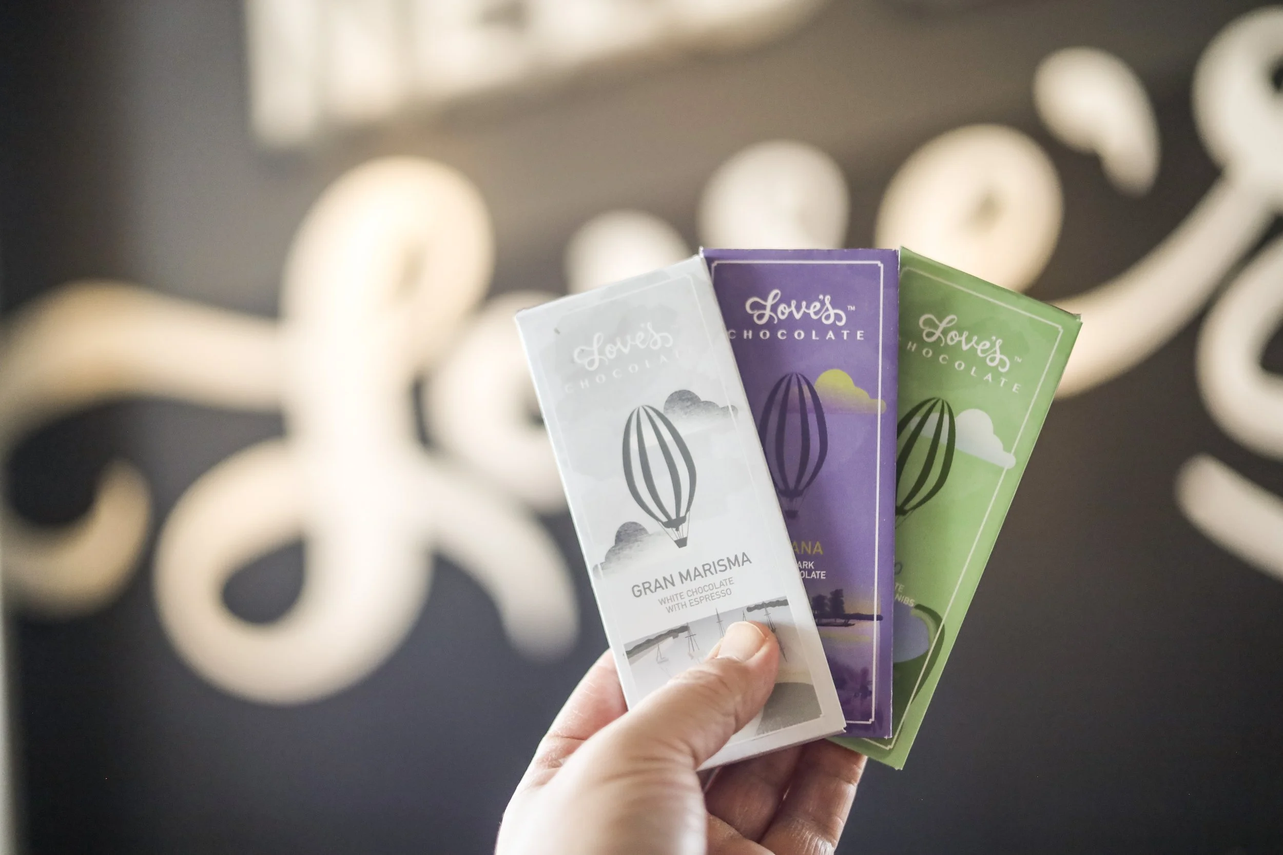 Hand holding three colorful chocolate bars with a mural background.