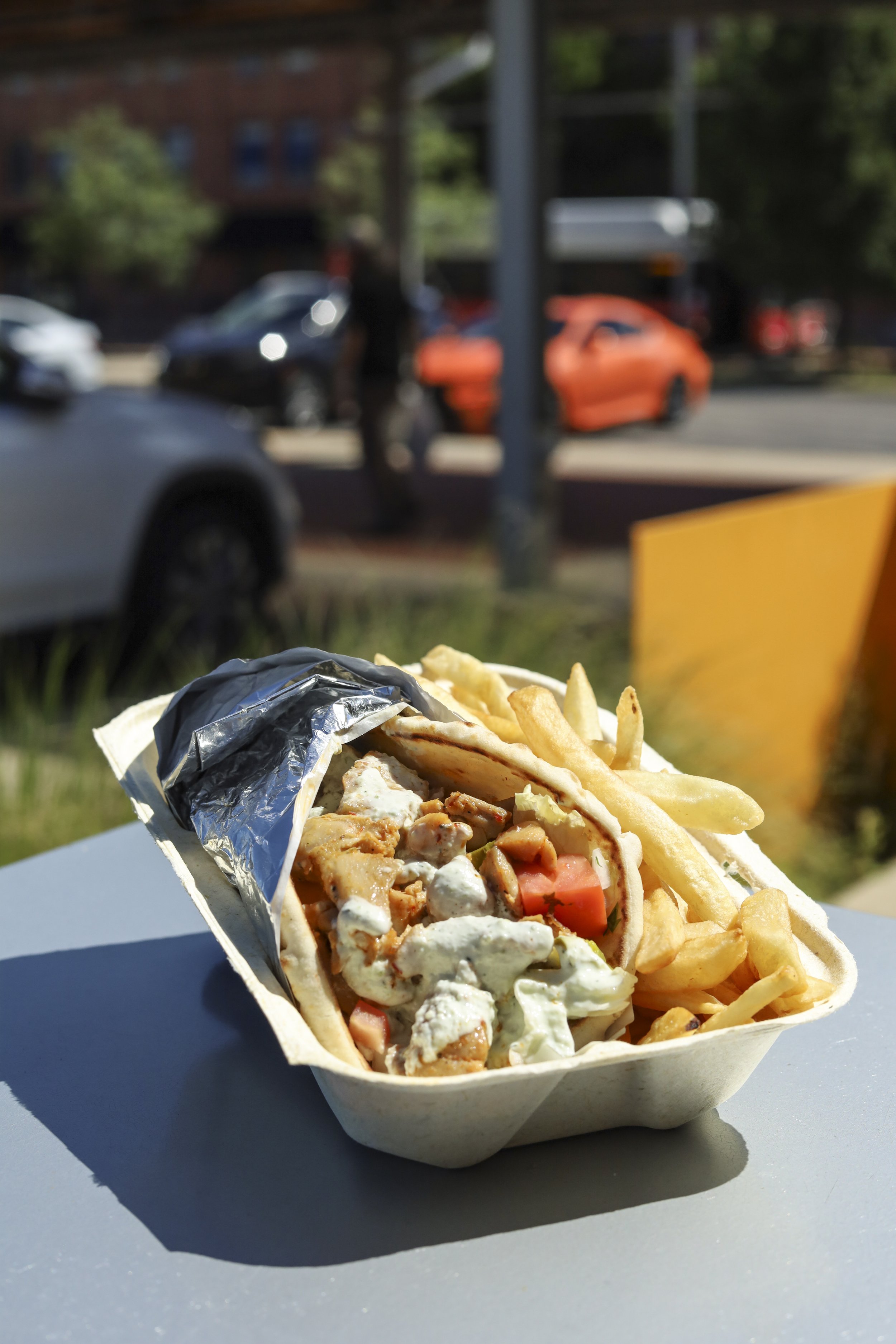 A takeout container with a gyro sandwich and French fries.