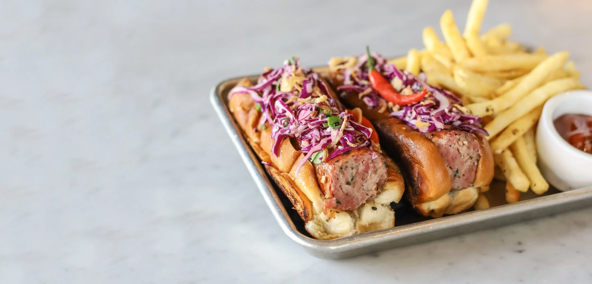 Metal tray with loaded sausages and fries.