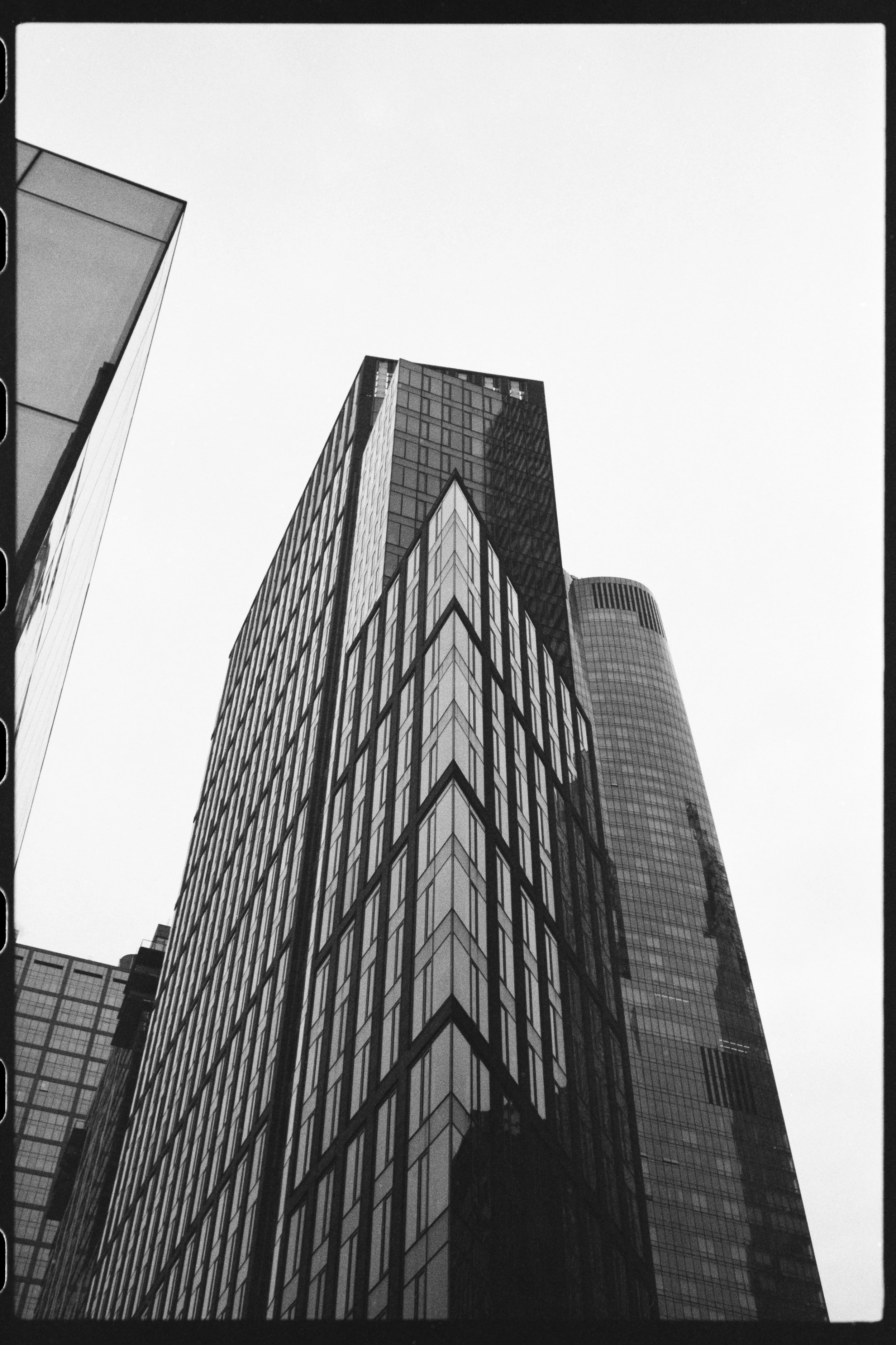 Black and white photograph of modern skyscrapers with glass facades, viewed from below against the sky.
