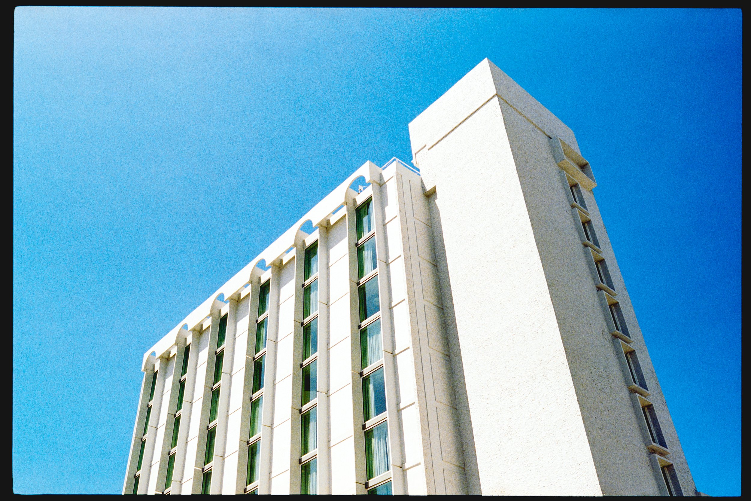 A tall white building with multiple green-tinted windows and decorative elements under a clear blue sky.