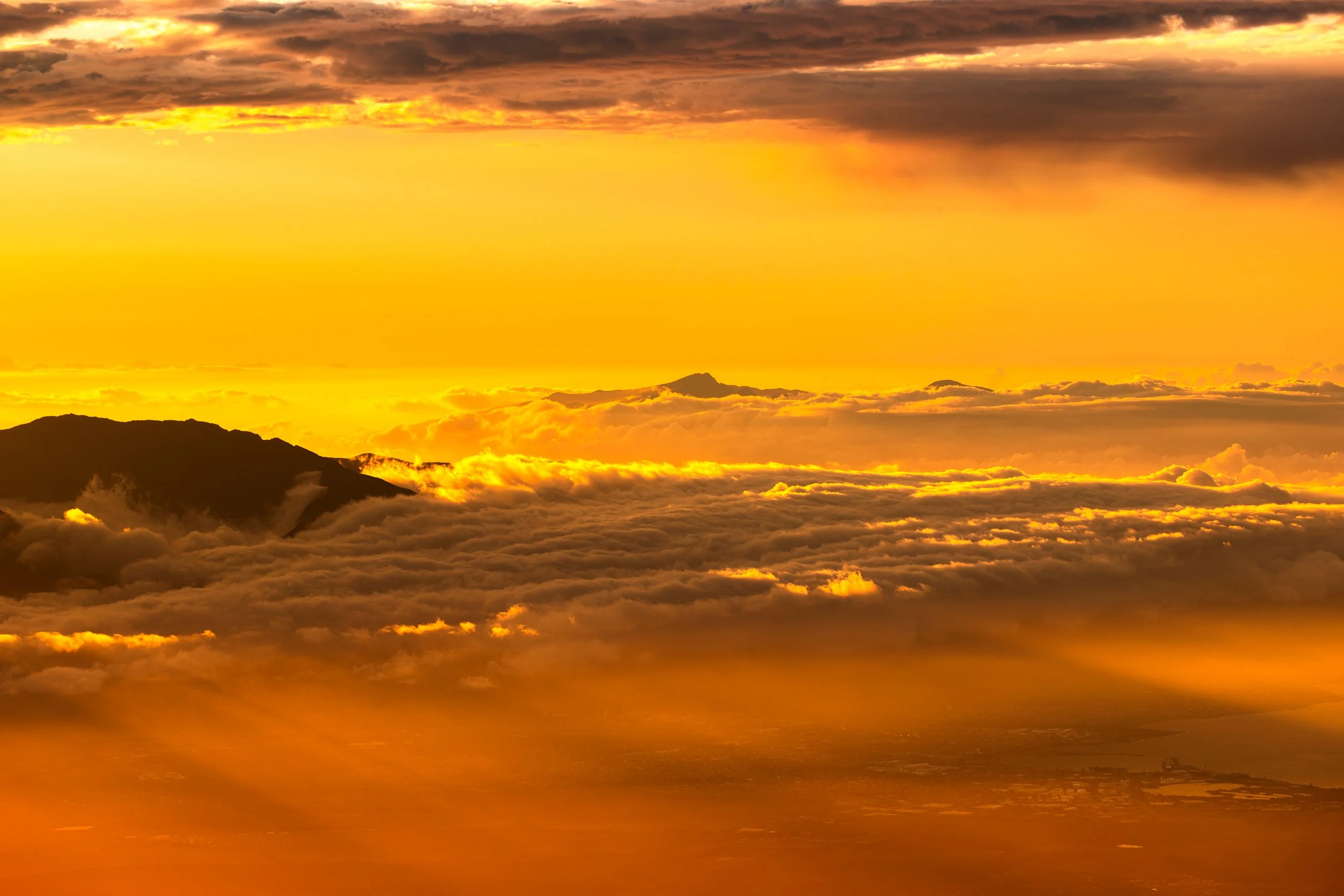 A stunning sunset or sunrise over a mountain range, with vibrant orange and yellow hues illuminating the sky and reflecting on the clouds below.