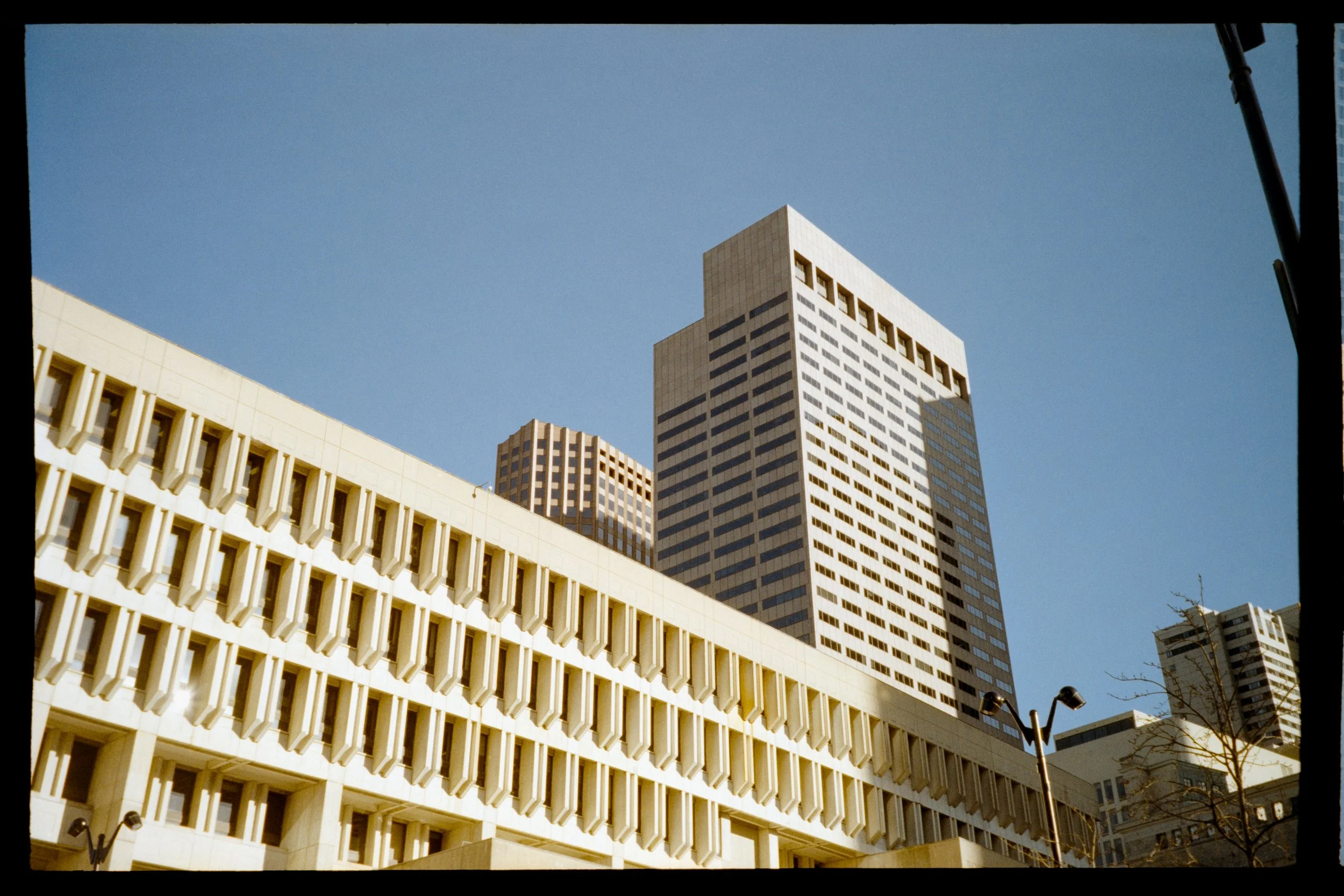Modern cityscape with tall skyscrapers and a blue sky, viewed from below.