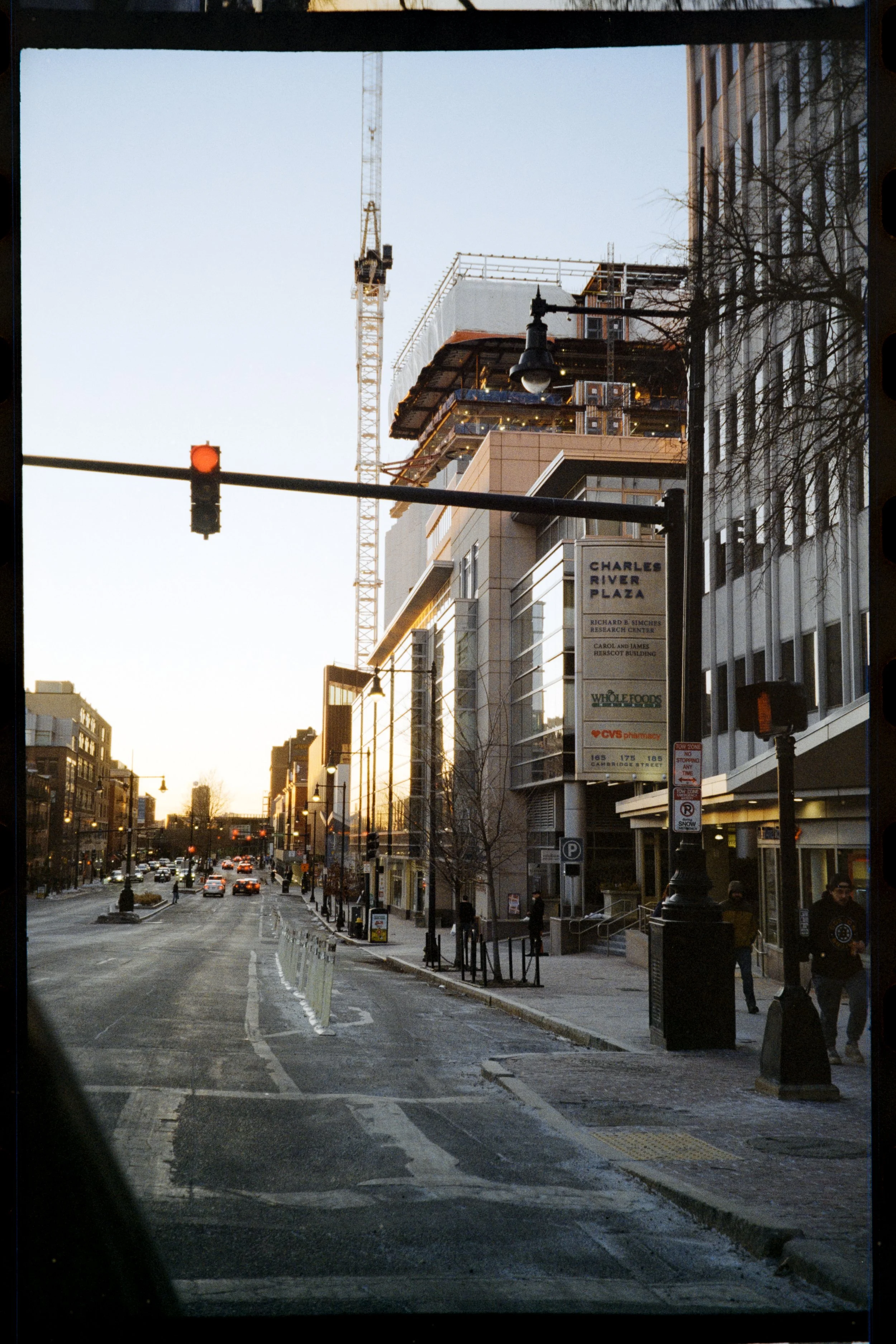 City street scene during sunset with traffic, buildings including Charles River Plaza, construction crane on top of a building, streetlights, and pedestrians.