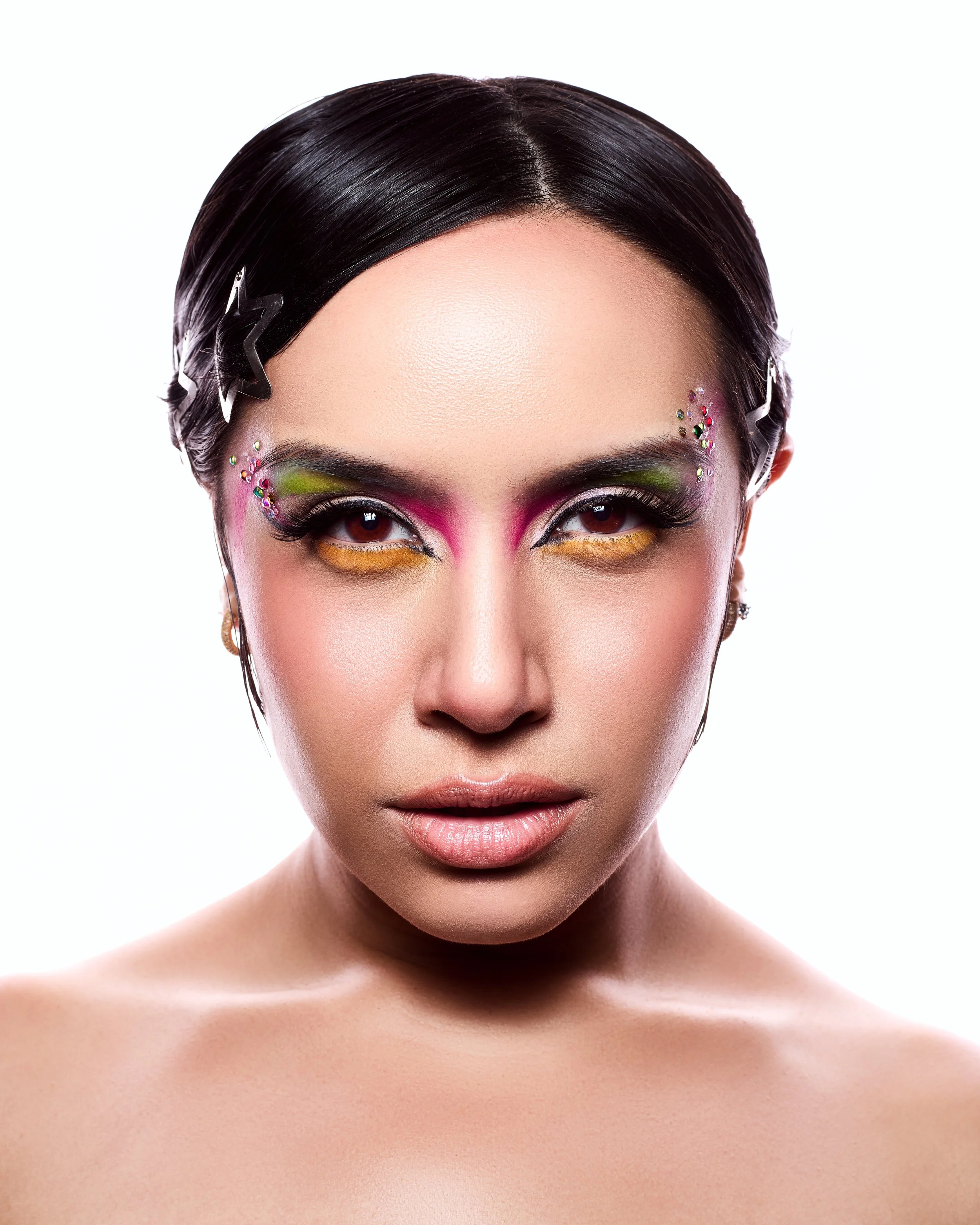Close-up of a woman with colorful, artistic makeup and dark, styled hair decorated with star-shaped hair clips.
