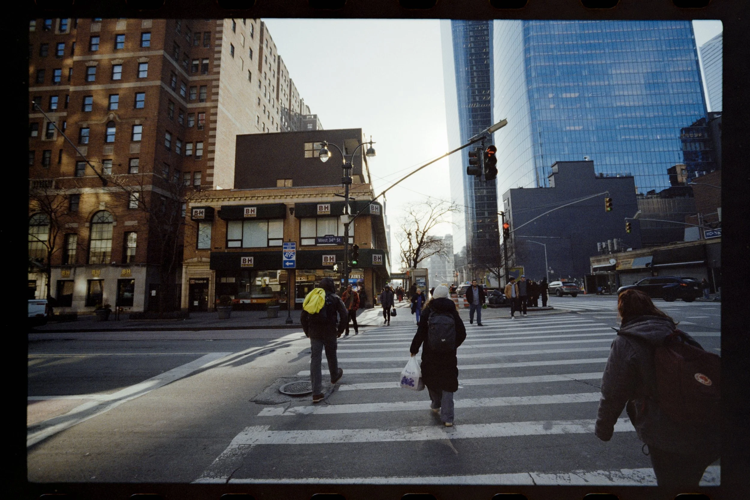 People crossing the street at a busy city intersection with tall buildings and traffic lights.