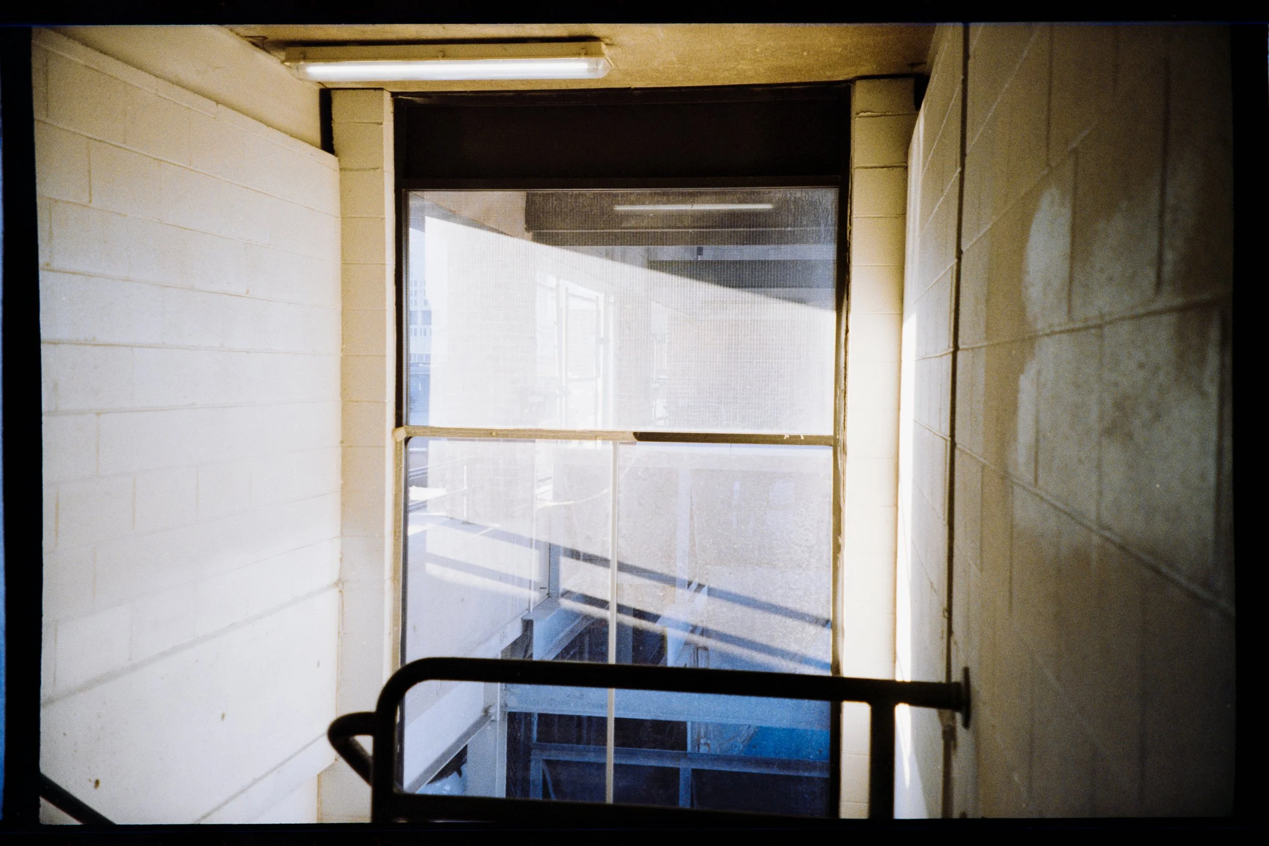 View through a glass door showing a staircase leading downward, with a partial view of the building exterior and a cityscape in the background.