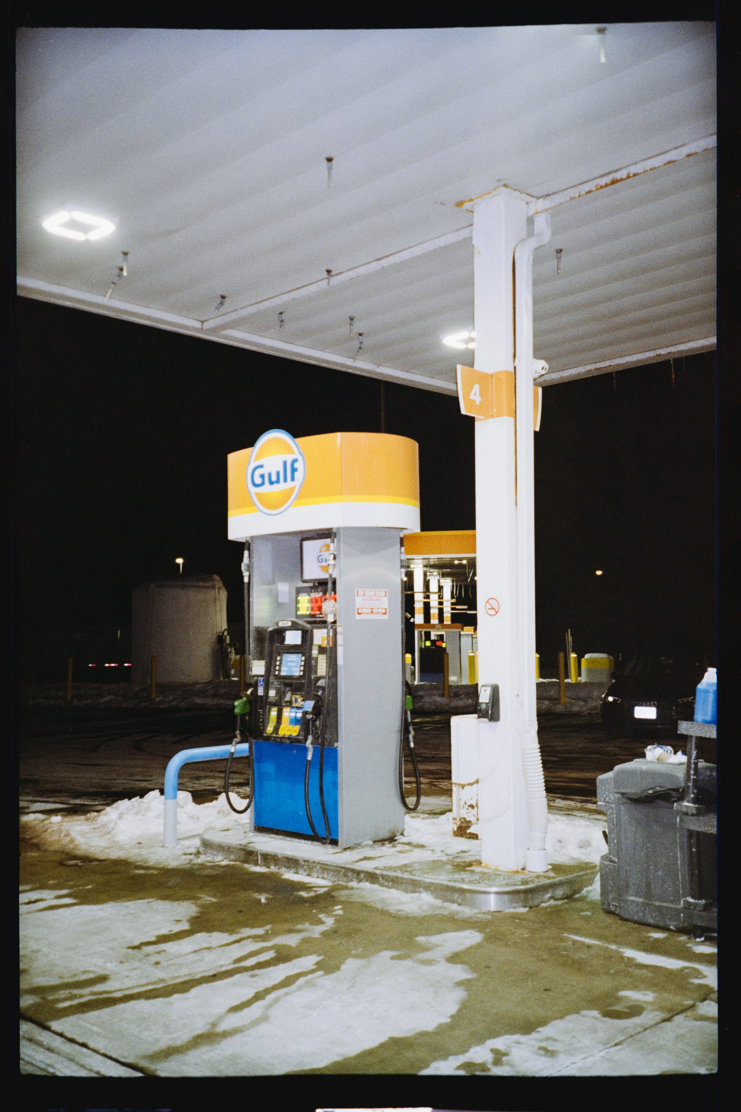 A Gulf gas station at night with a pump, a small snowy area in the foreground, and a dark sky.